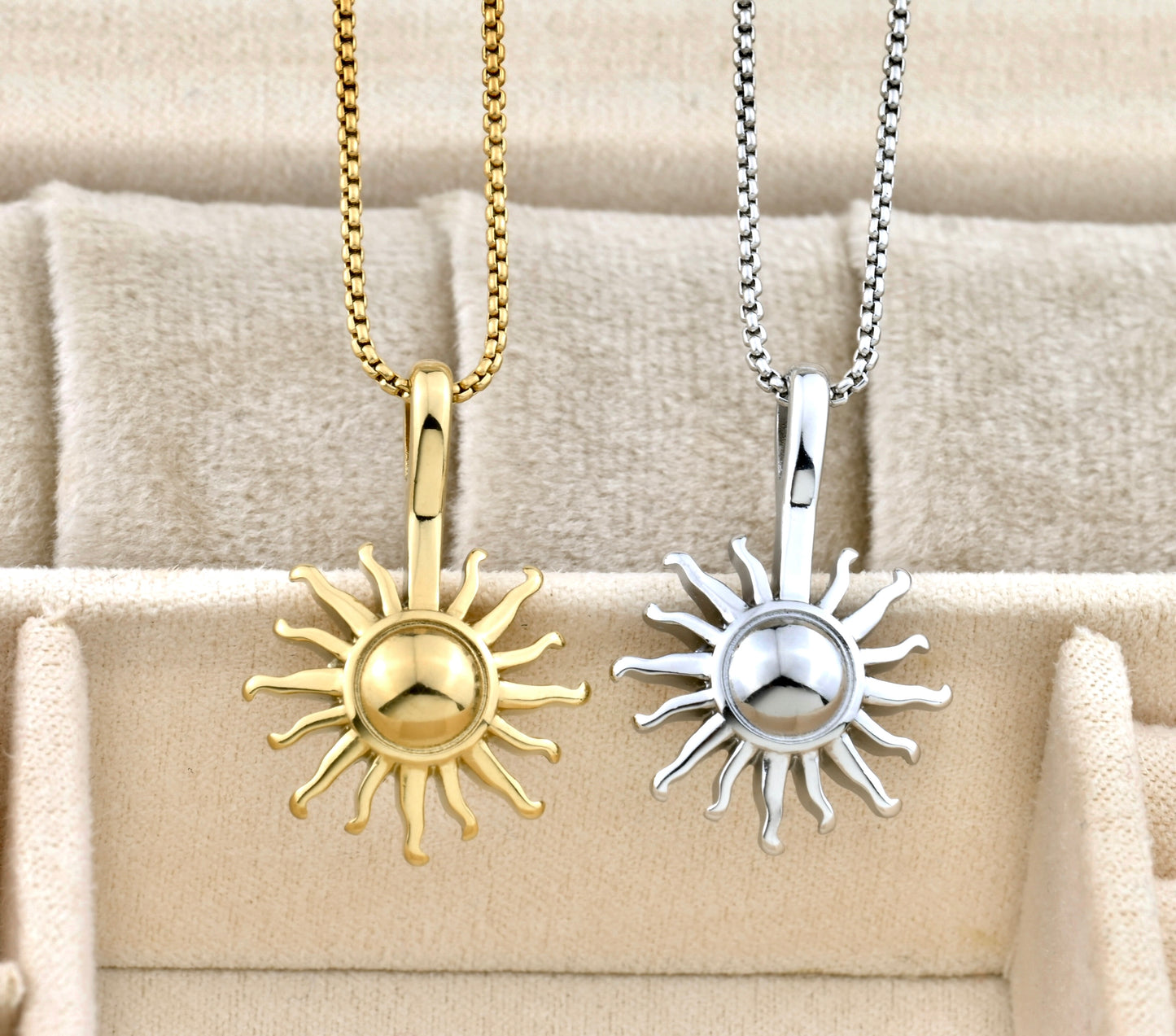 Two sun-shaped pendants, one gold and one silver, on beige fabric.