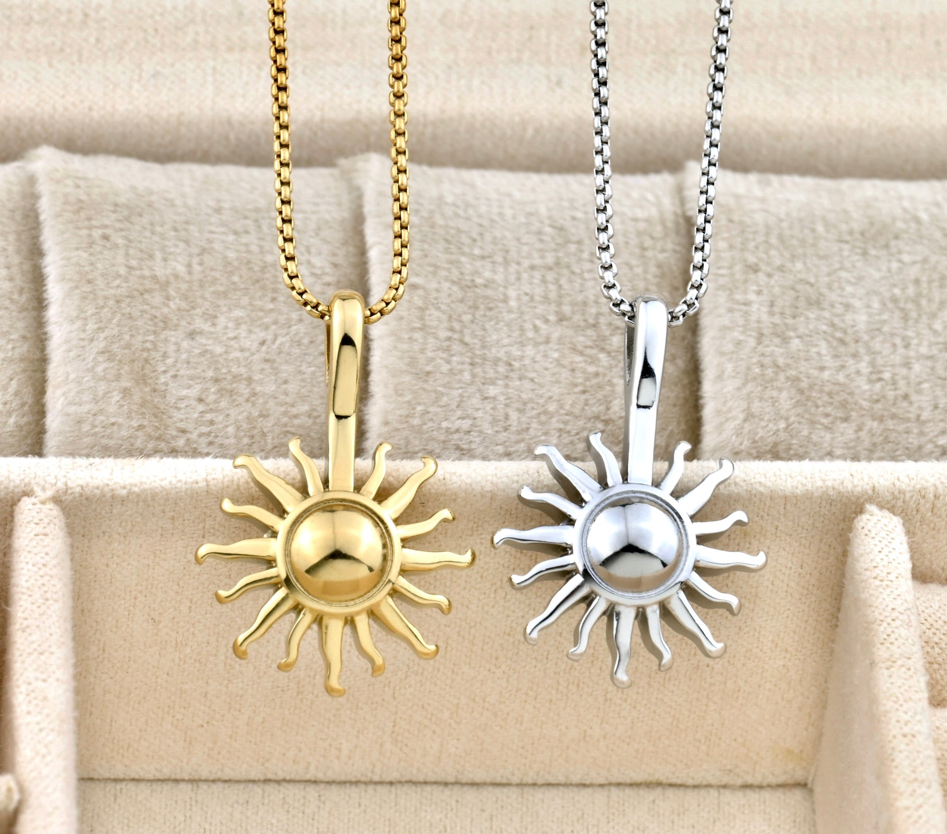 Two sun-shaped pendants, one gold and one silver, on beige fabric.
