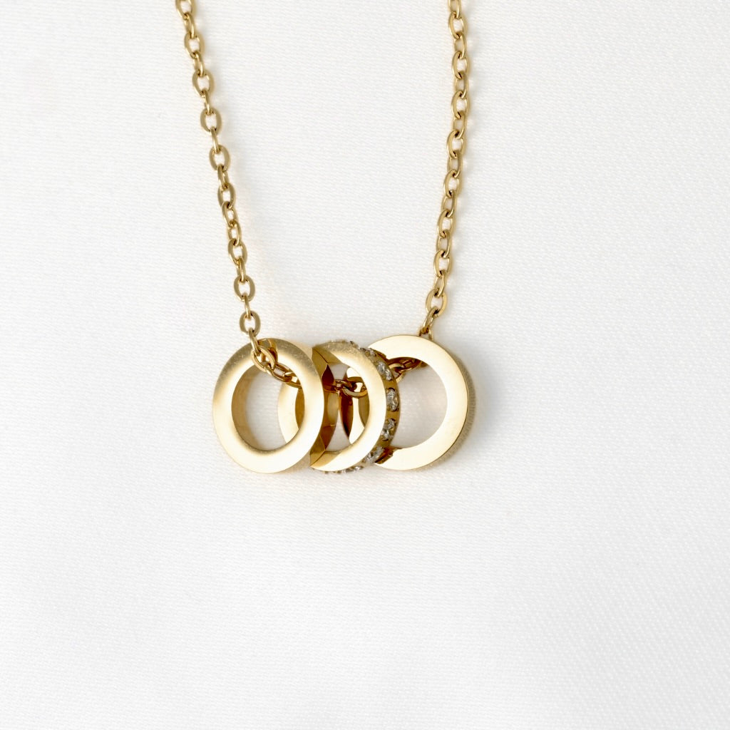 A gold chain necklace featuring three circular ring pendants, displayed on a clean white background.