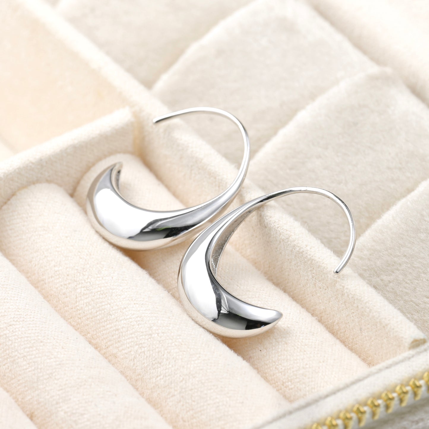 Medium-sized silver hoop earrings on a beige jewelry box