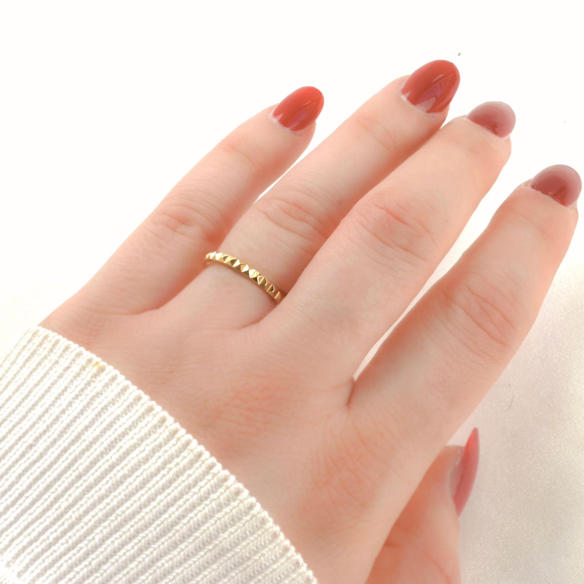 Hand wearing a gold pyramid ring with a plain background
