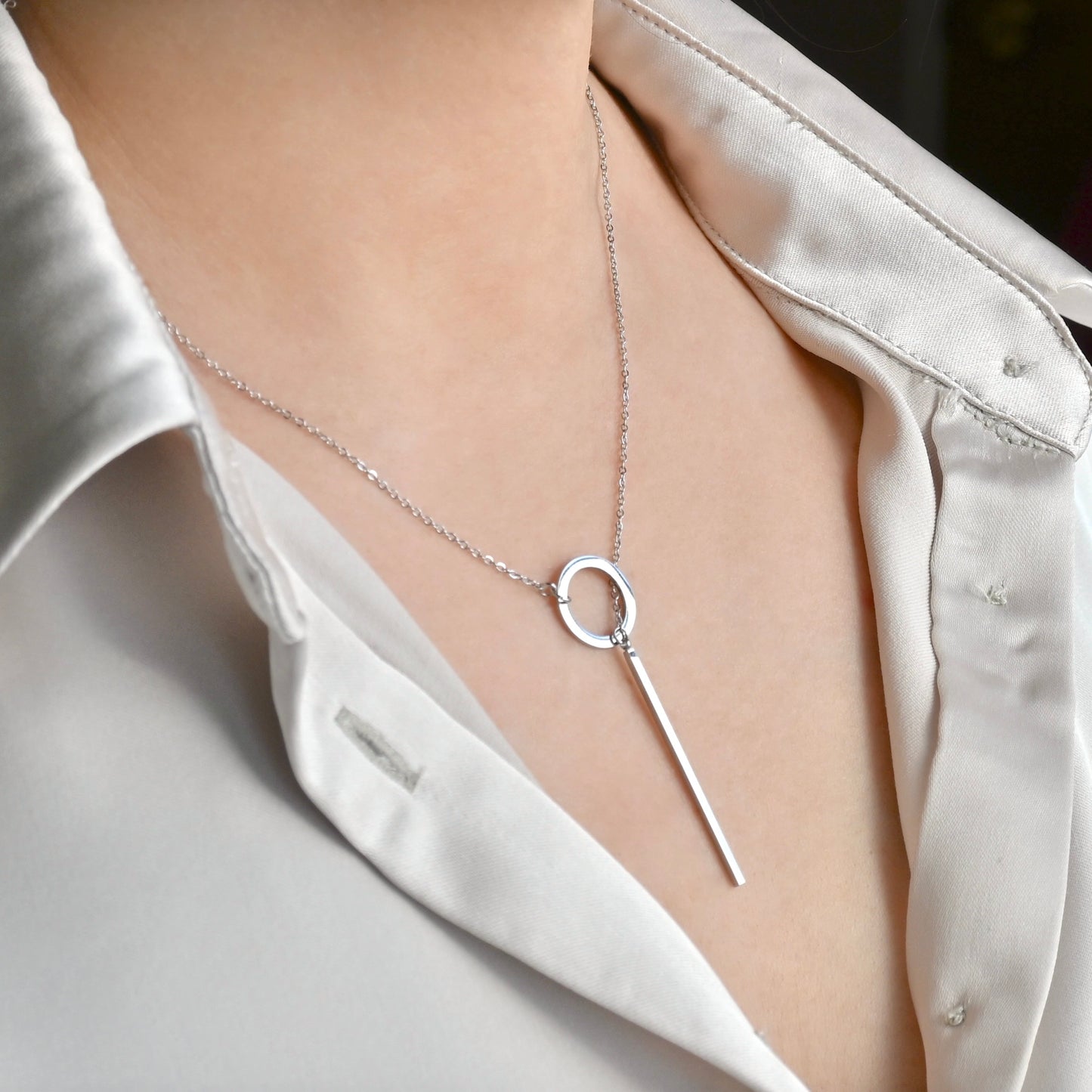 Silver circle and bar clasp necklace on a person wearing a white shirt.