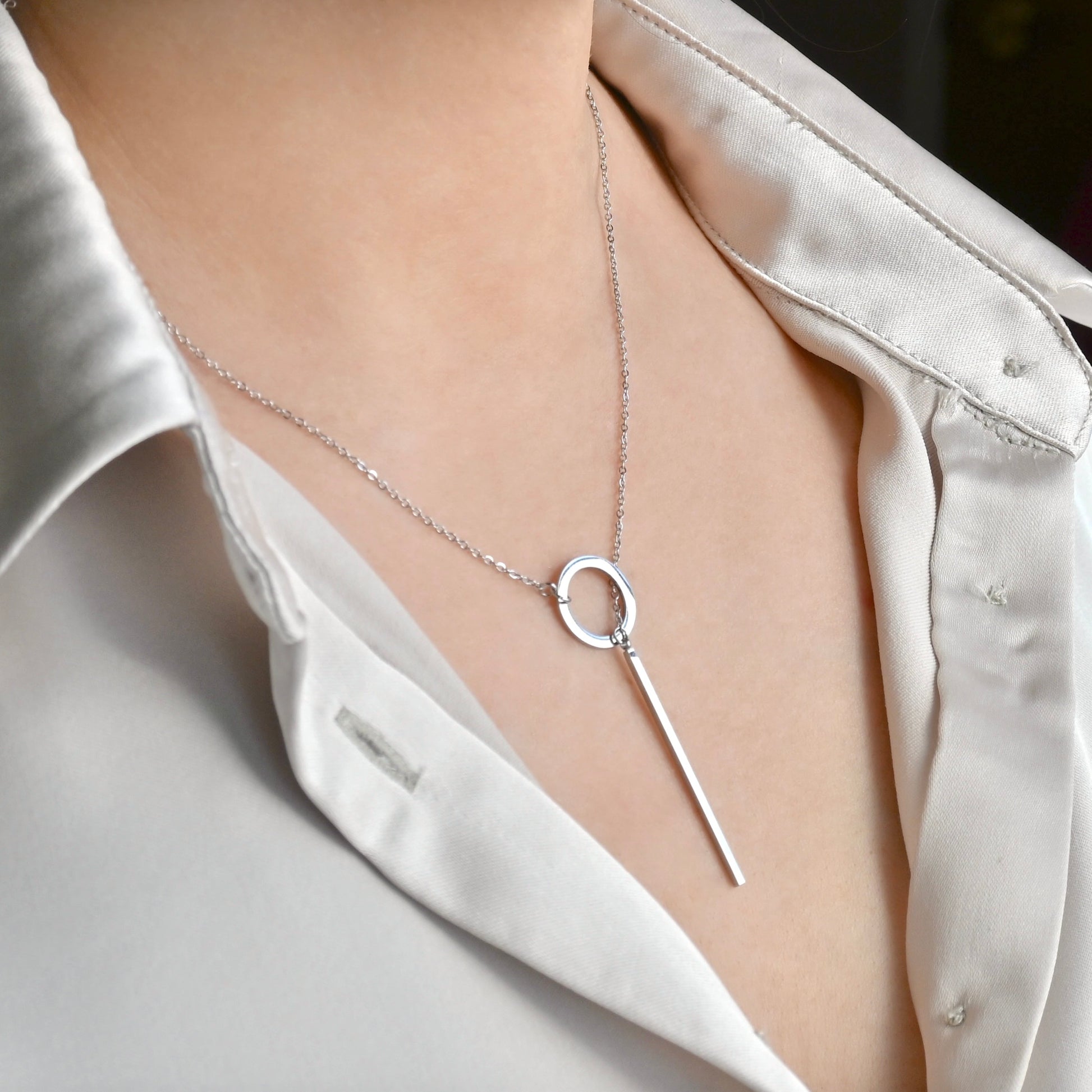 Silver circle and bar clasp necklace on a person wearing a white shirt.