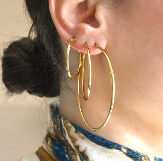 Classic thin gold hoop earrings, 60mm, 40mm and 30mm sizes worn by a person with a neutral background