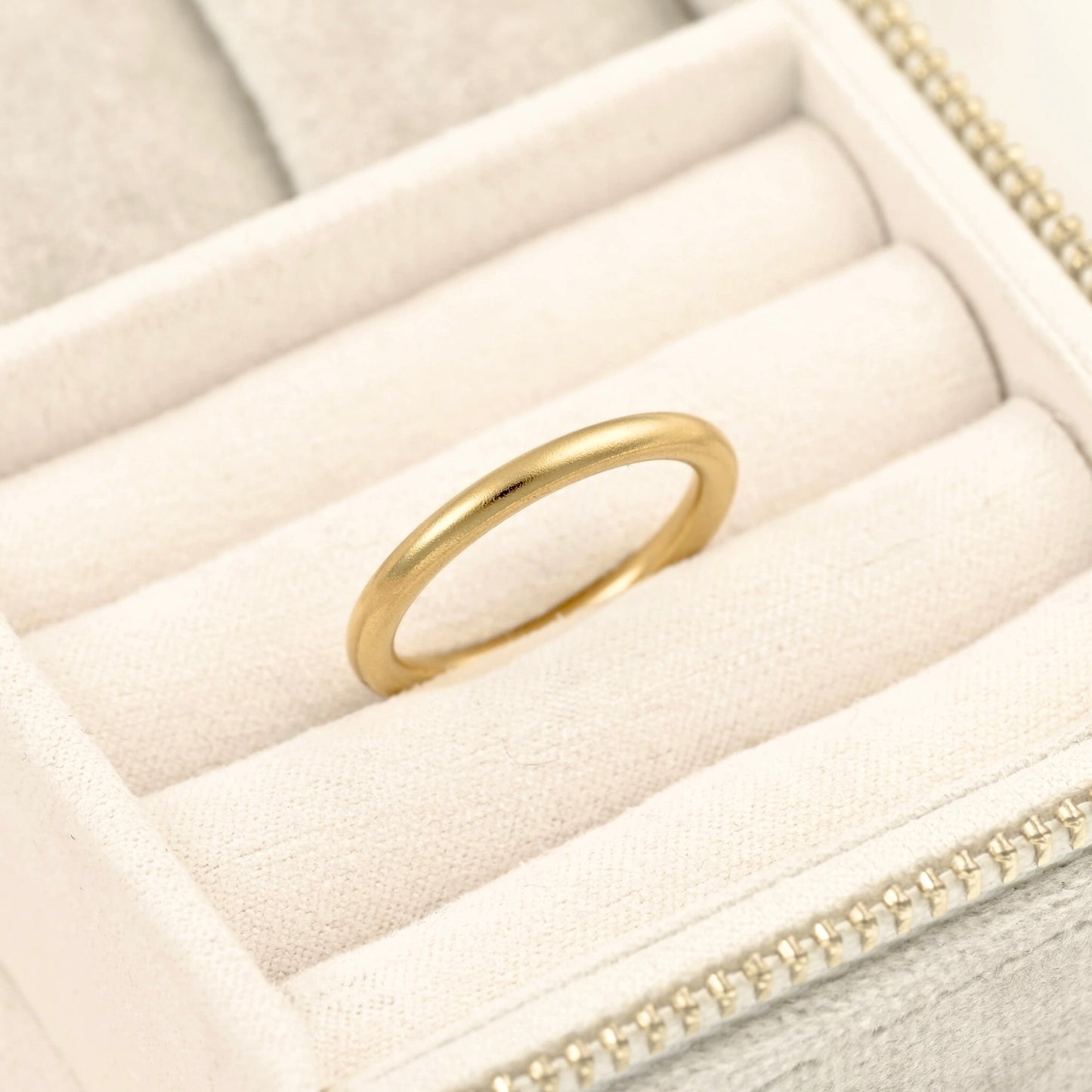 Angled view of slim rounded wedding band in beige jewelry box.