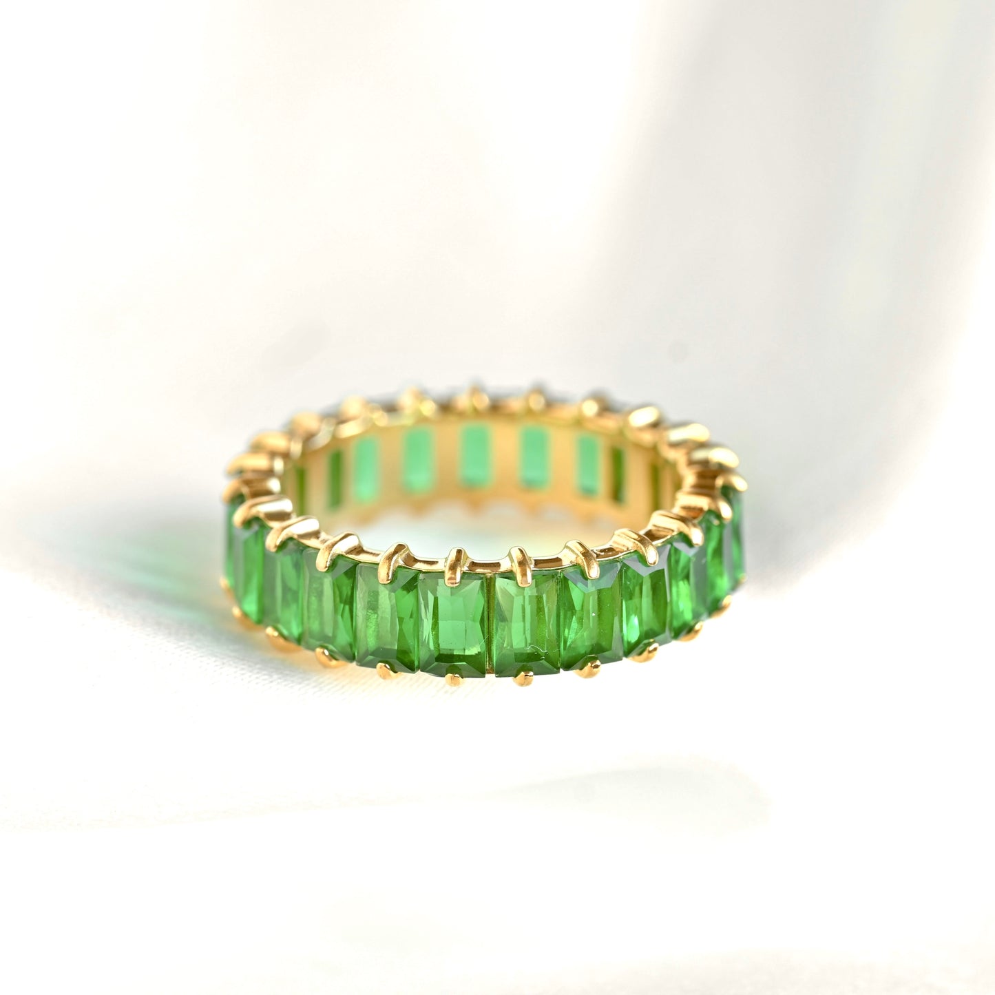 Gold ring with green baguette gemstones on a white background