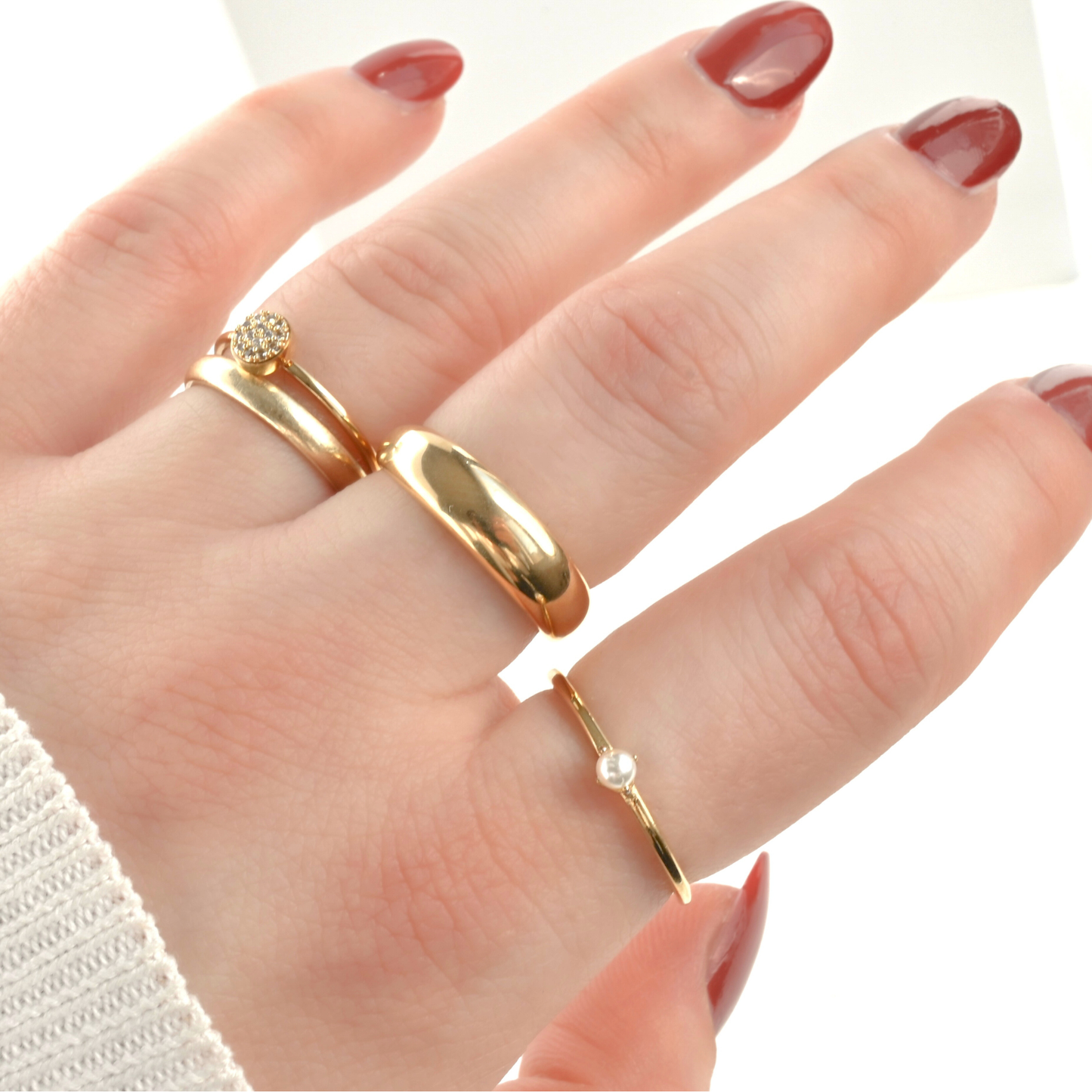 Hand wearing a stack of gold rings with different designs with a plain background