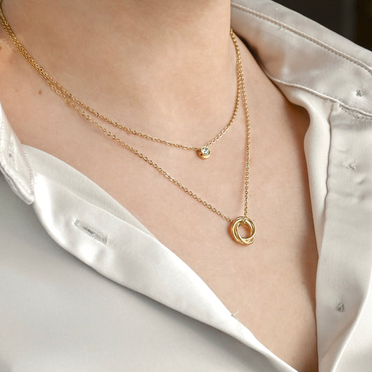 Layered gold necklace with circular pendants on a person wearing white satin shirt