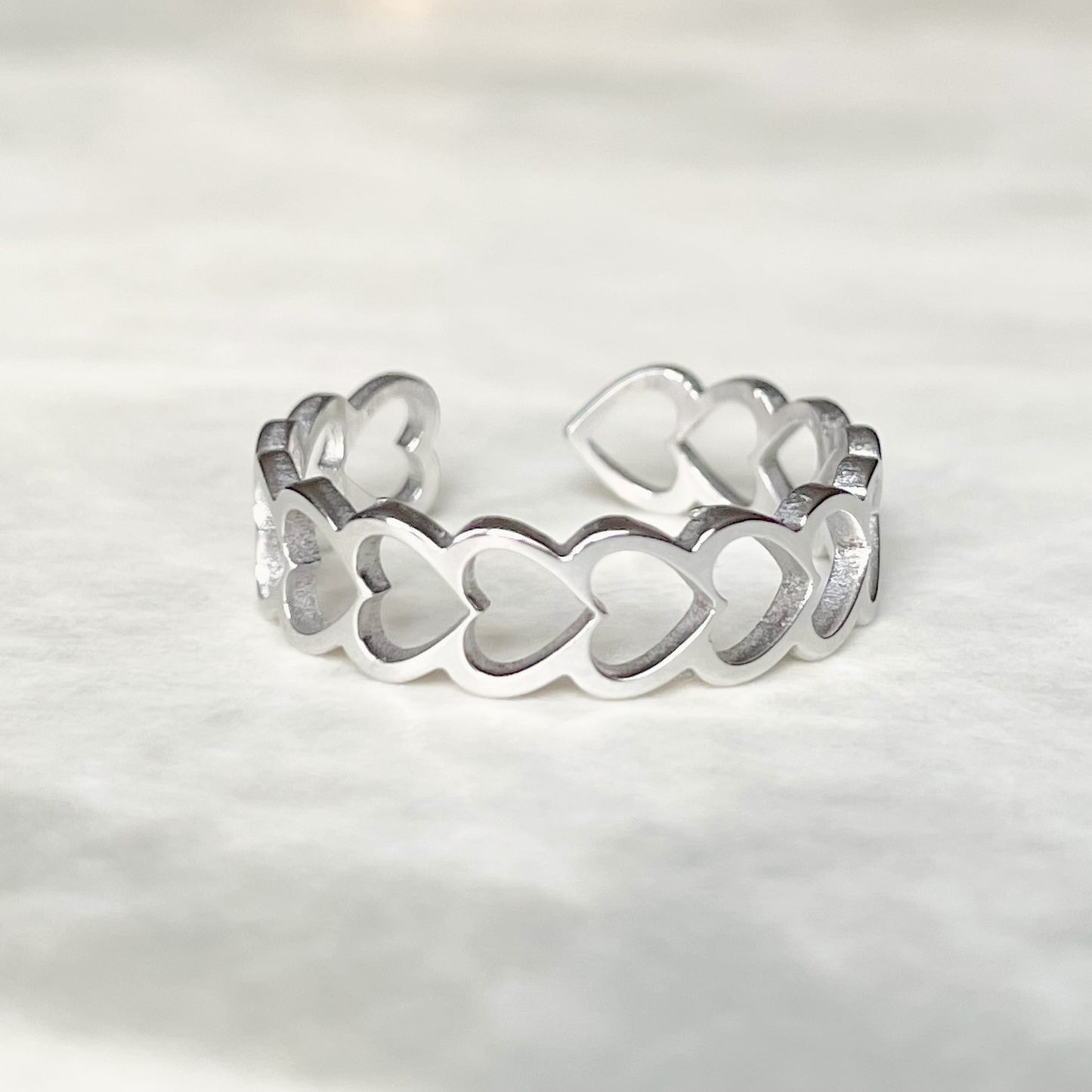 Front view of open back silver  heart ring on a light gray background