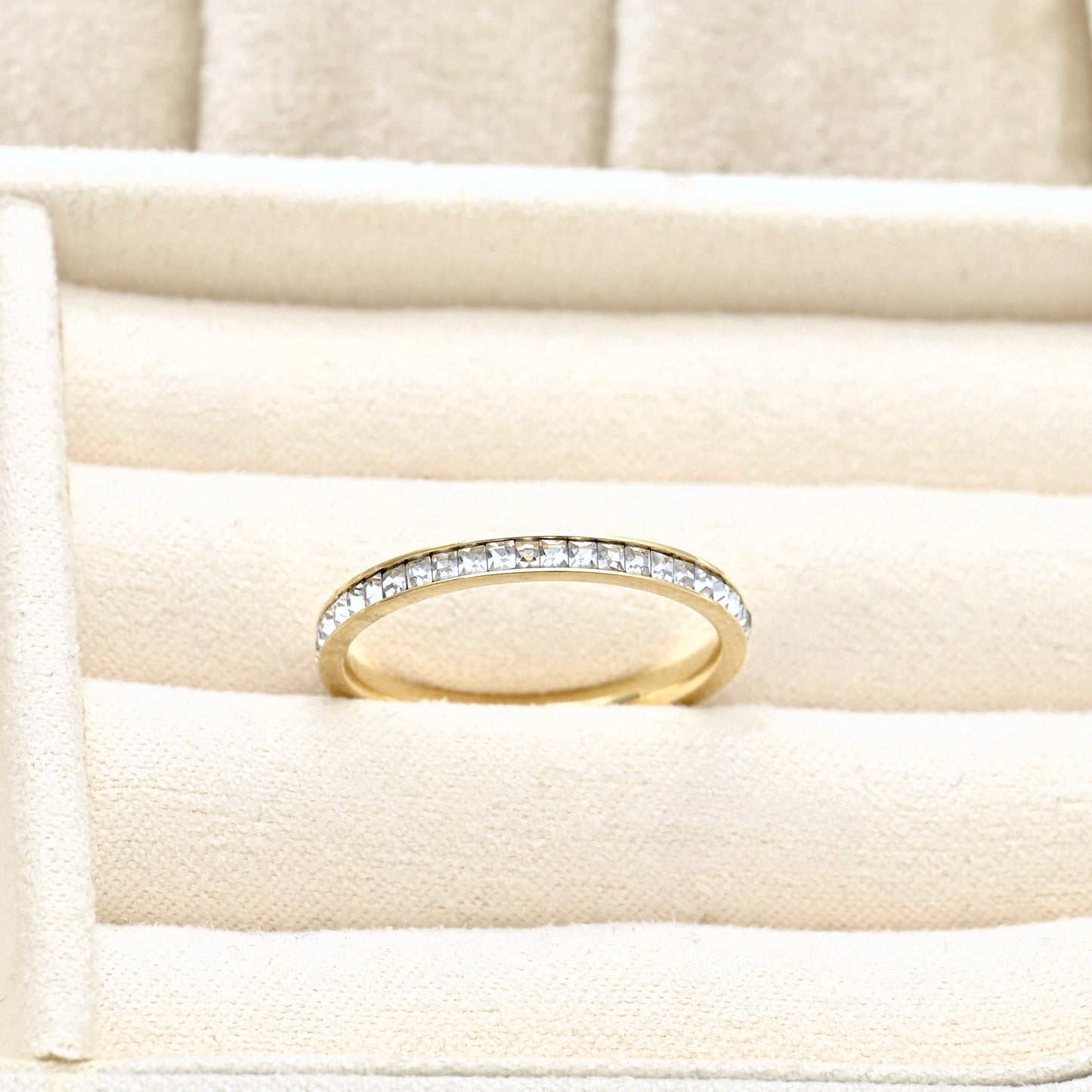 Front top view of a thin gold eternity diamond ring with channel set squre cubic zirconia stones in a beige jewelry box