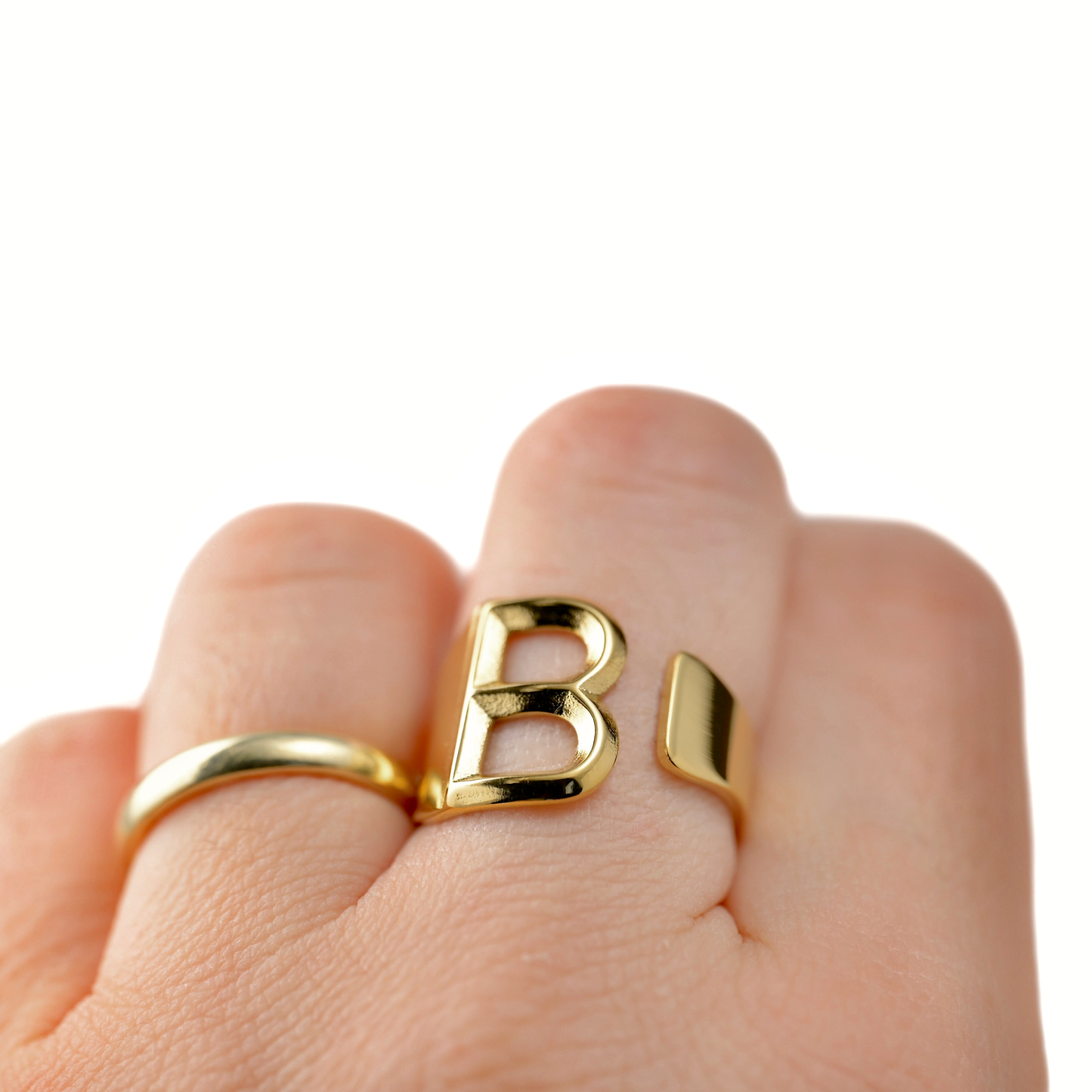 Thick Gold ring with letter 'B' on a finger against a white background