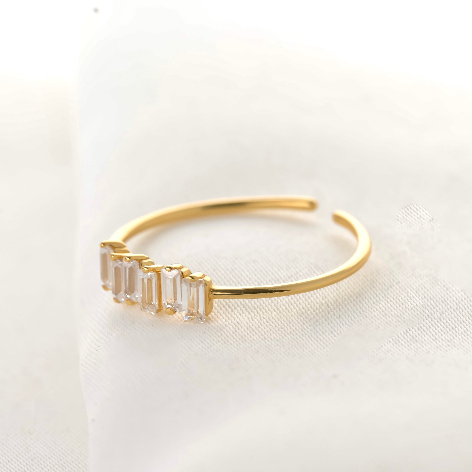 Side view of gold baguette cluster ring on a light fabric background