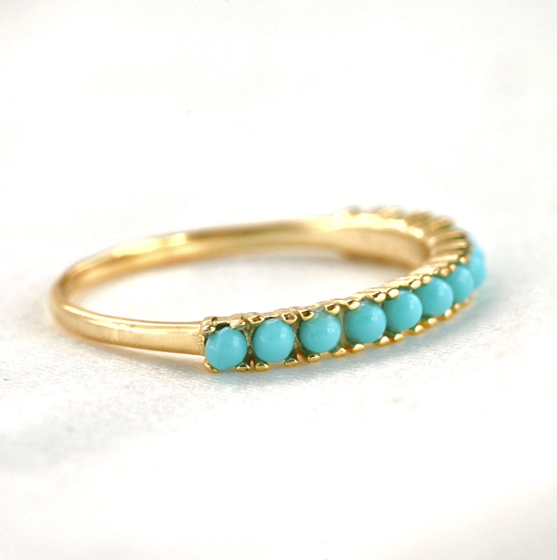 Gold half eternity ring with turquoise stones on a white background