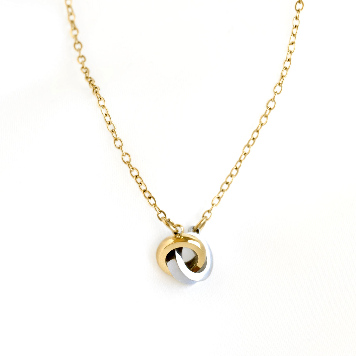 A delicate gold chain necklace featuring a pendant with two interlocking swirls in polished gold and silver, set against a clean white background.