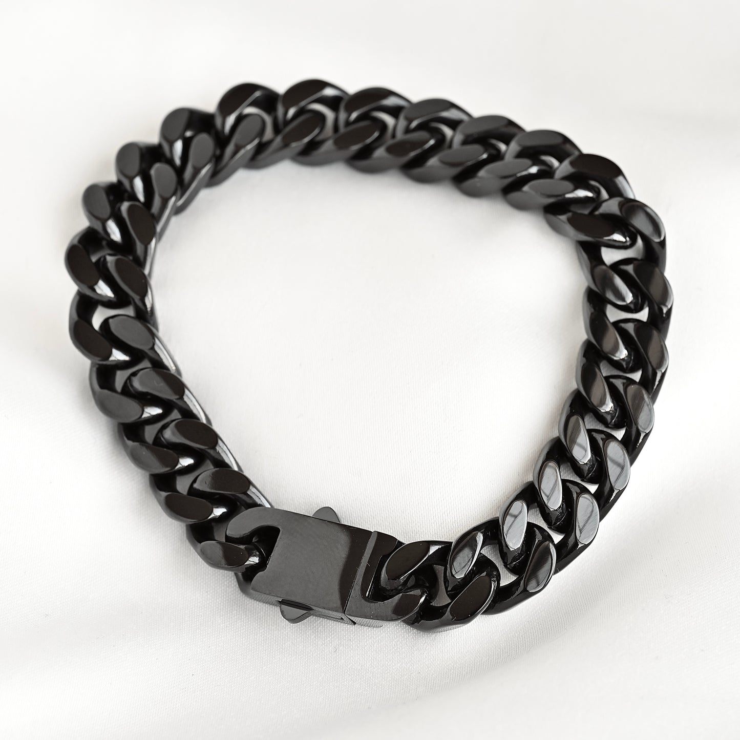 A black glossy Cuban link chain bracelet with a matching black clasp, photographed on a white fabric background.