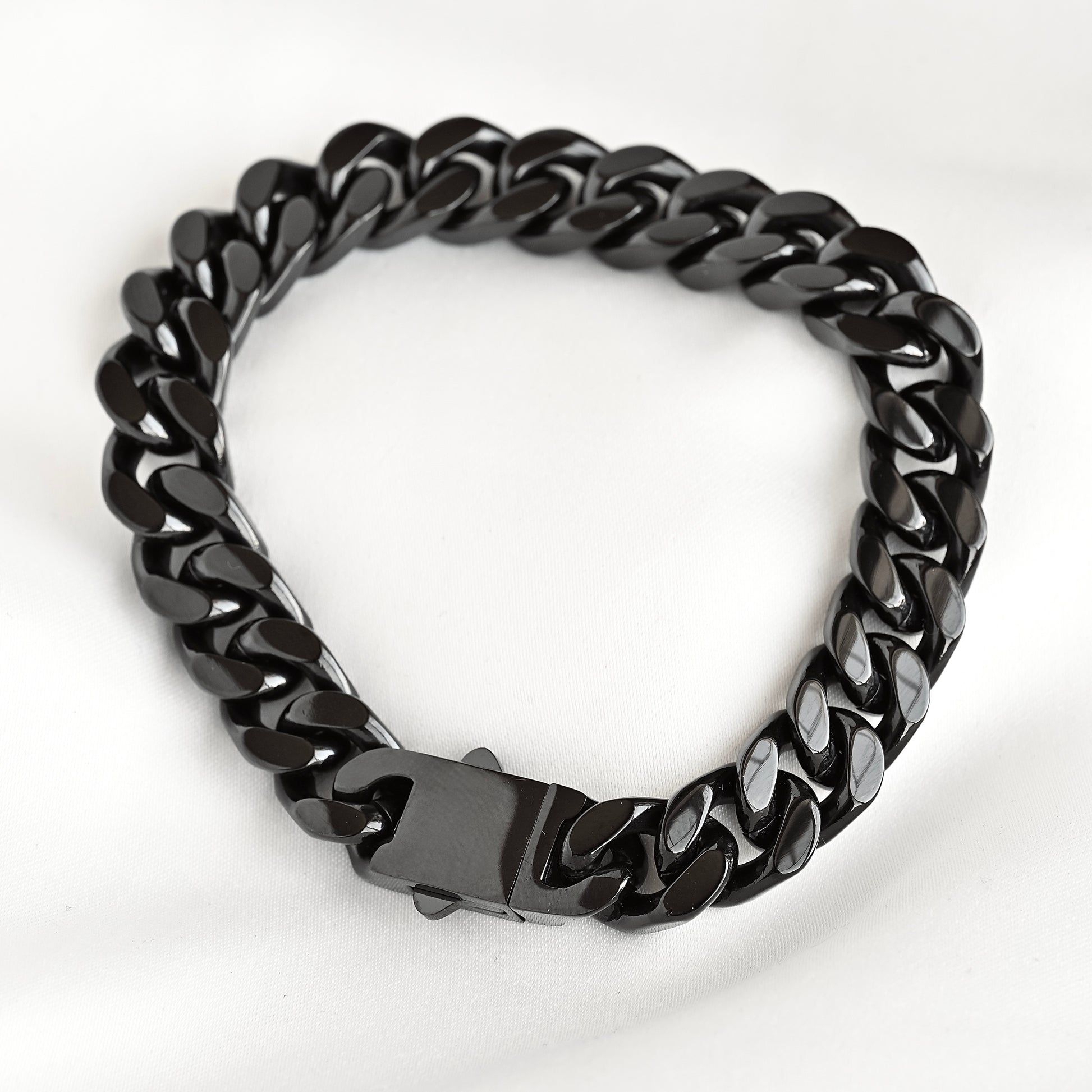 A black glossy Cuban link chain bracelet with a matching black clasp, photographed on a white fabric background.