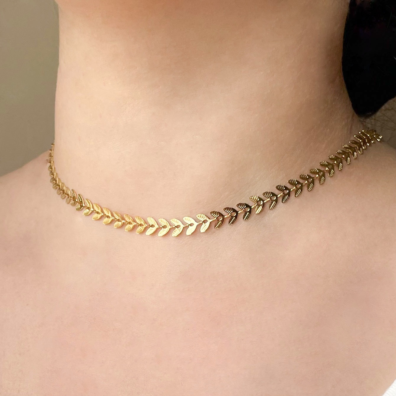 Gold leaf choker necklace with textured leaf links on a person's neck against a neutral background