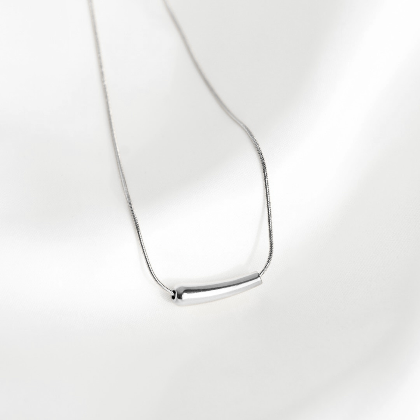A minimalist silver necklace featuring a polished horizontal bar pendant on a delicate chain, displayed against a clean white background with soft shadows.