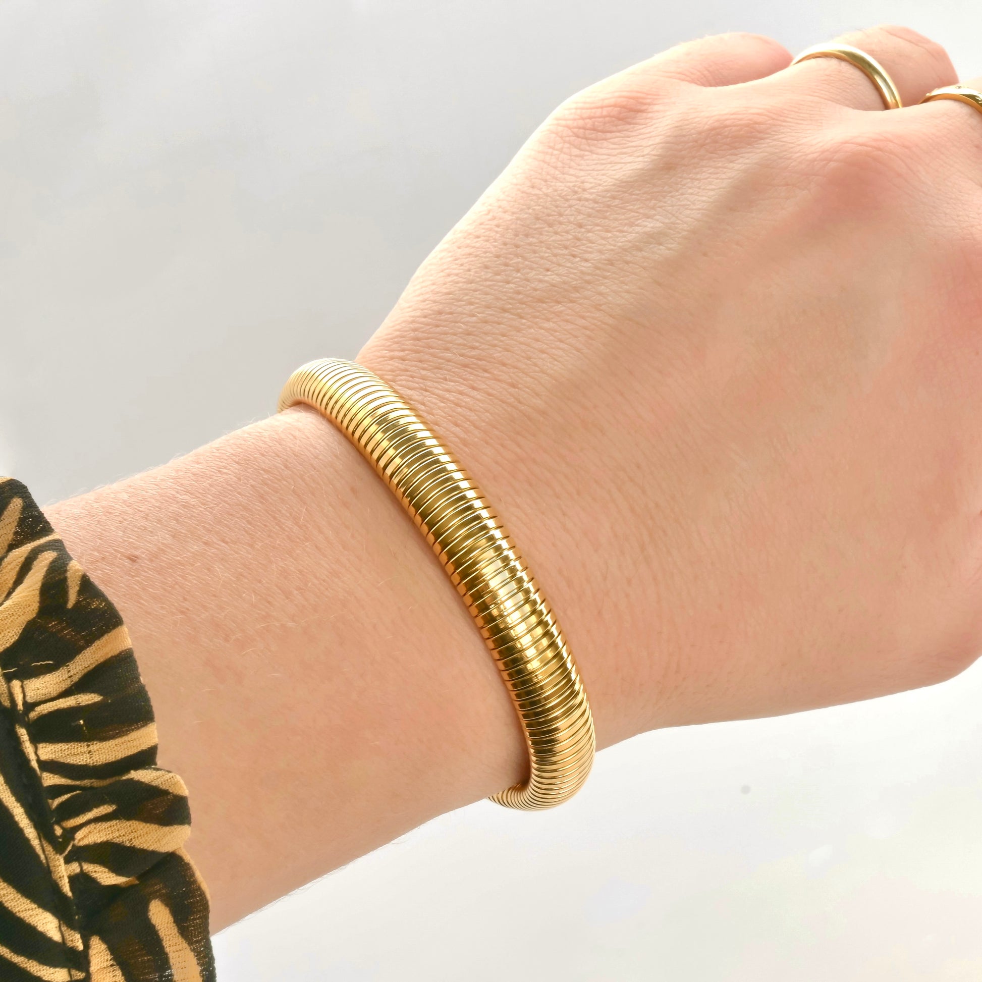 Ribbed gold bangle on a wrist with a plain background