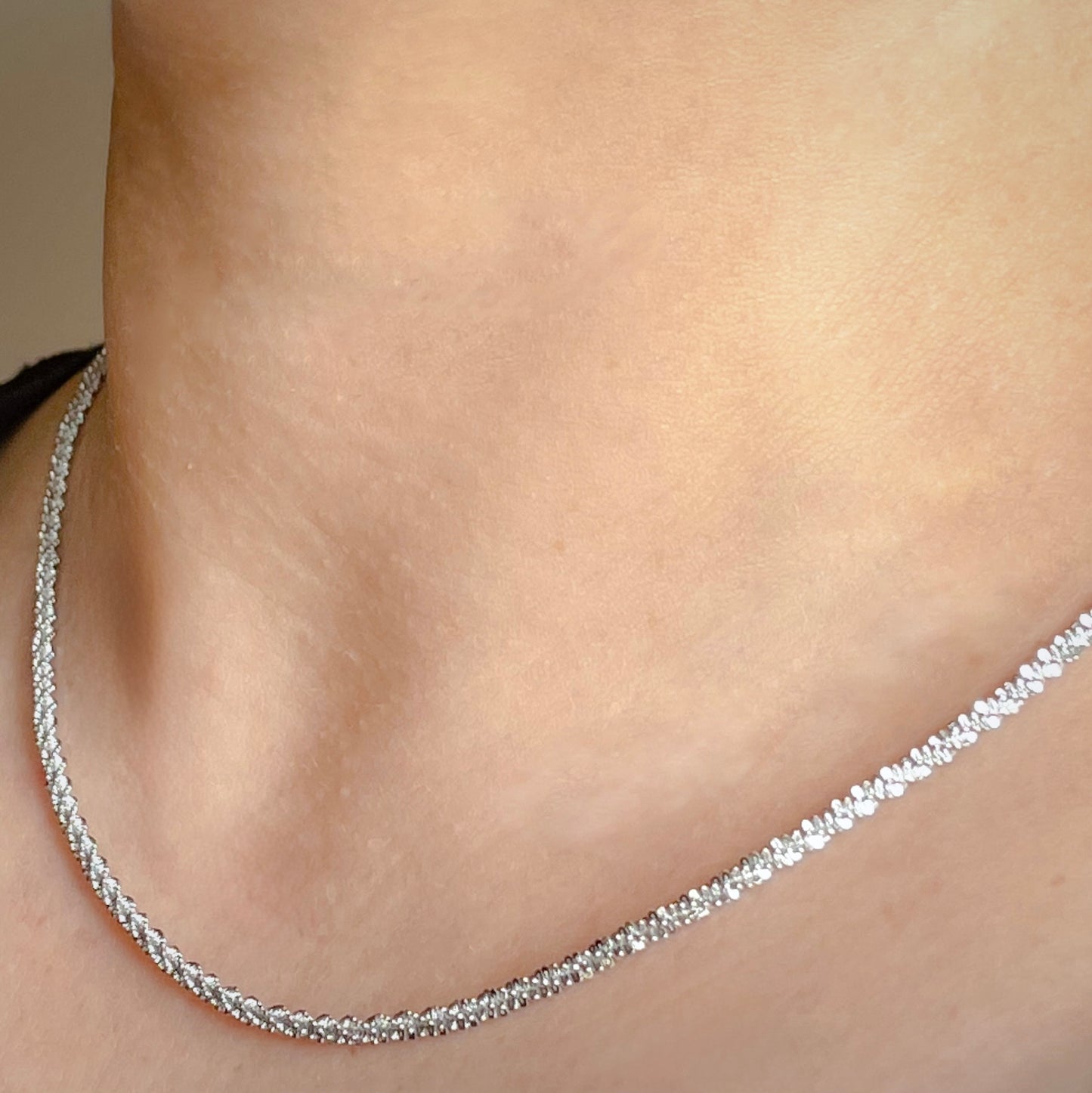 Silver necklace on a person's neck against a neutral background