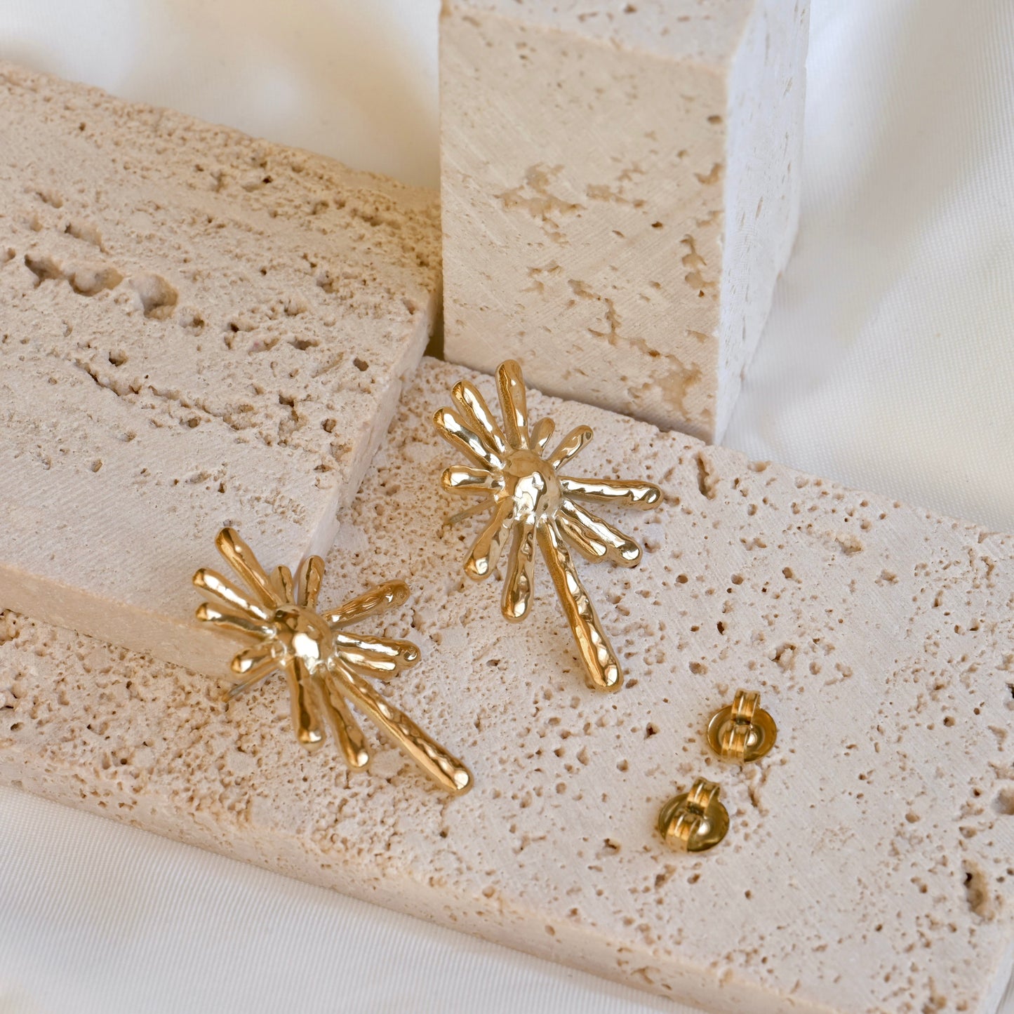 Gold starburst earrings on a textured beige surface