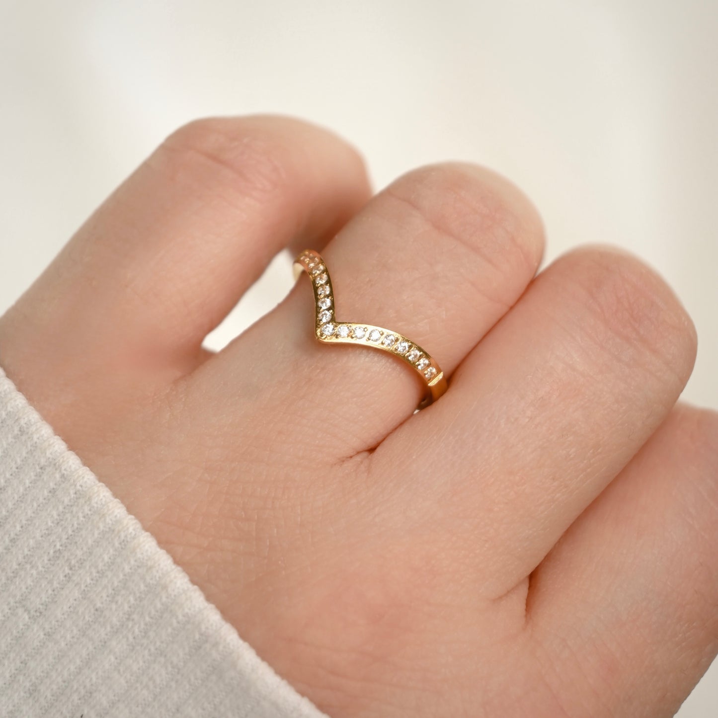 A gold V-shaped ring with small clear stones, worn on a person's finger.