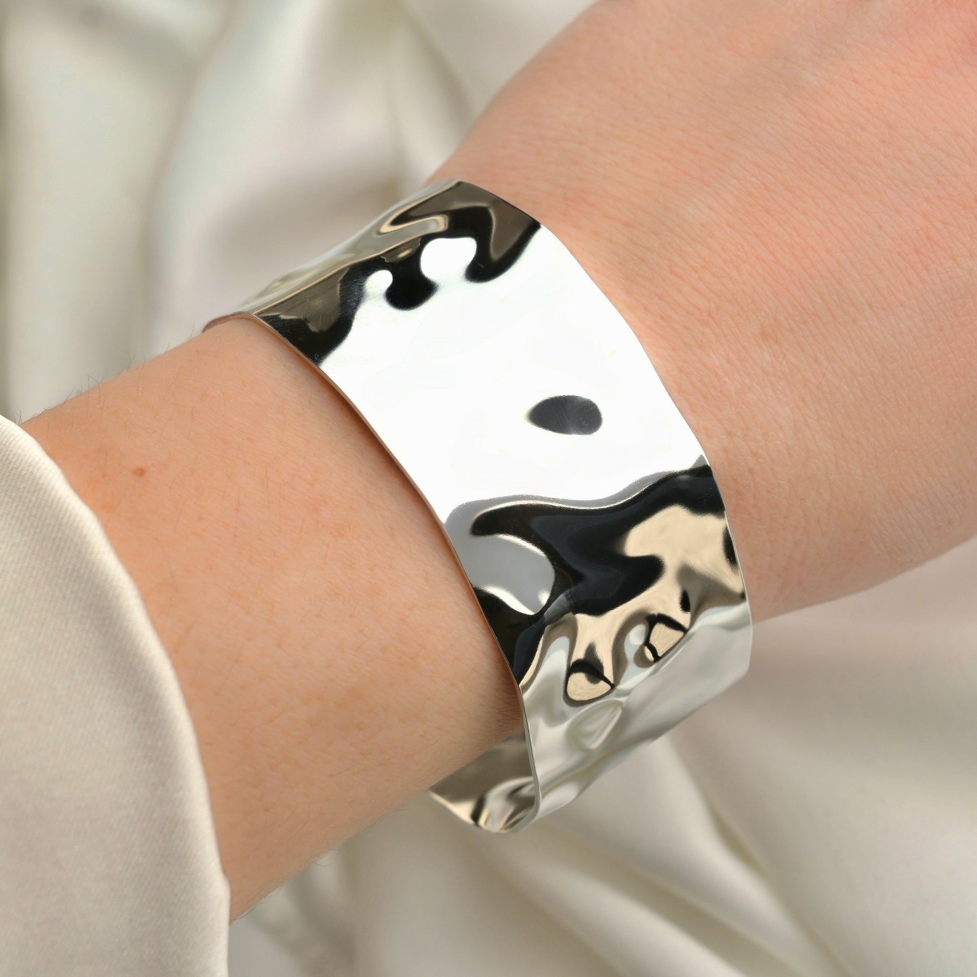 Silver cuff bracelet on a person's wrist against a neutral background