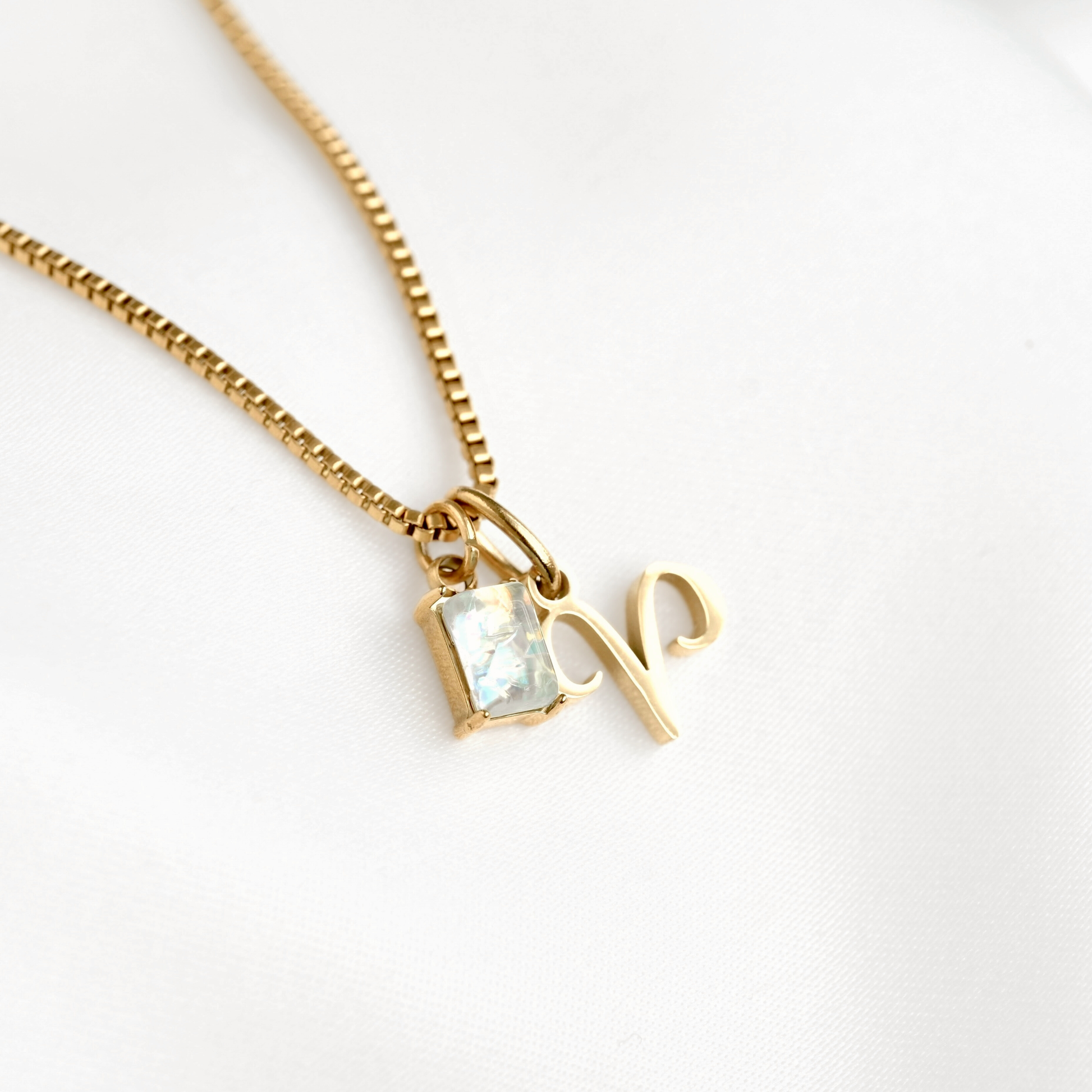 Gold box chain necklace with a small october birthstone and aries charm on a white background