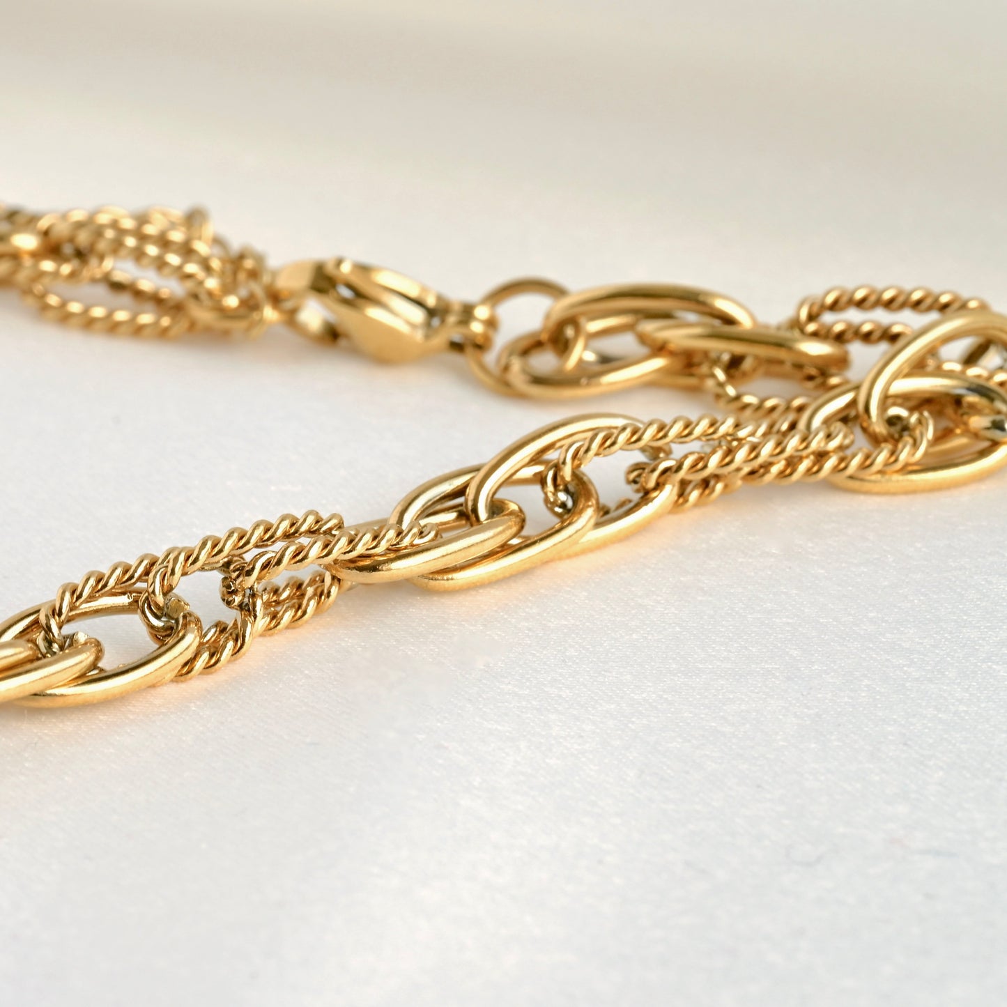 Close up view of interlocking smooth high polish and textured rope oval link chain in gold