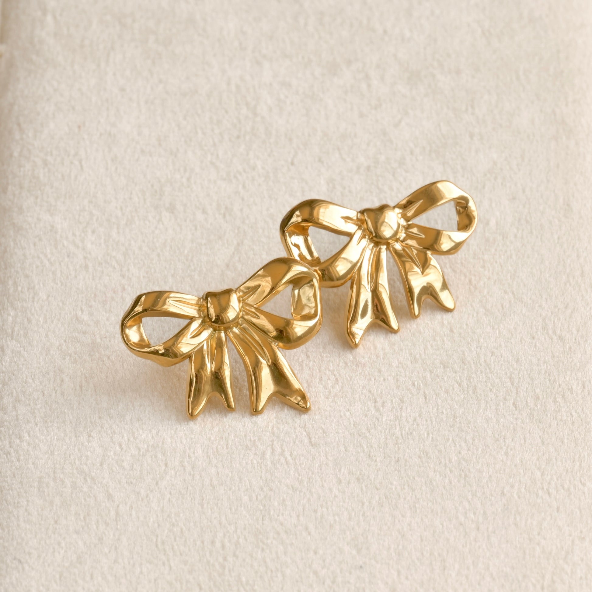 Gold bow-shaped earrings on a beige background