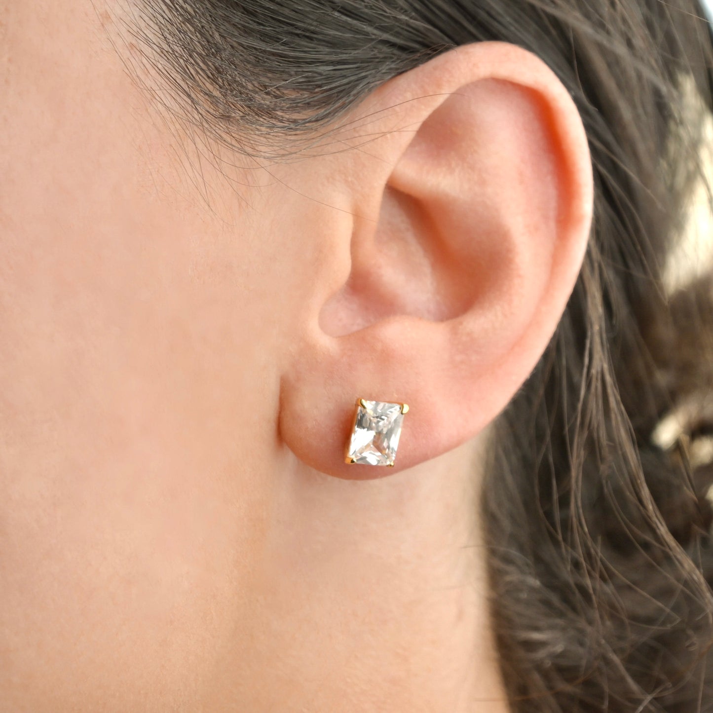 Close-up of an ear wearing a gold and clear gemstone stud earring.