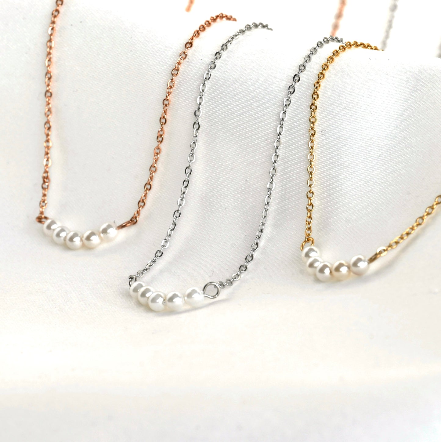 Three pearl necklaces with rose gold, silver, and gold cable chains on a white background