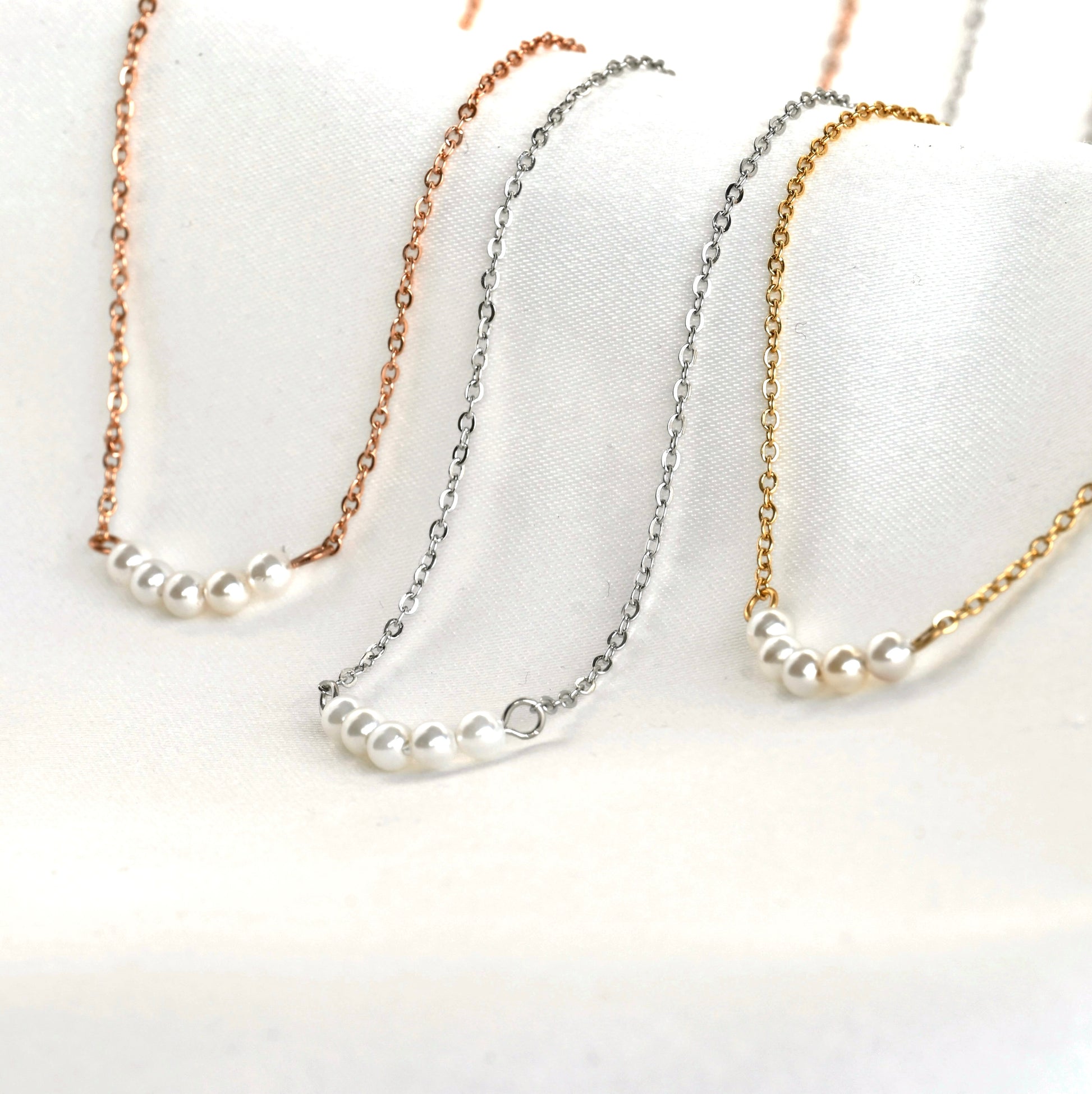 Three pearl necklaces with rose gold, silver, and gold cable chains on a white background