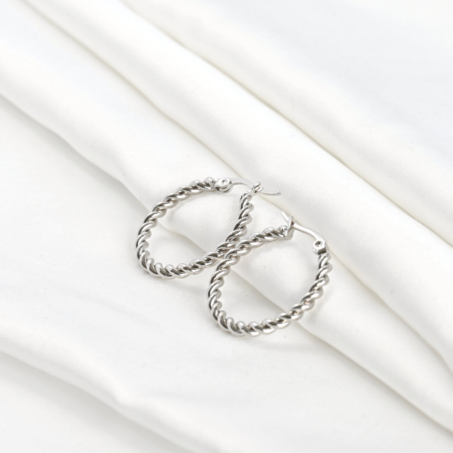 Wide angle view of silver twist  hoop earrings on a white fabric background