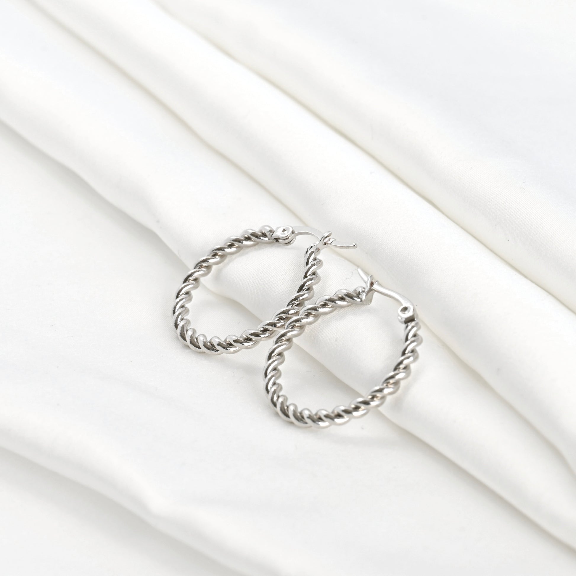 Wide angle view of silver twist  hoop earrings on a white fabric background