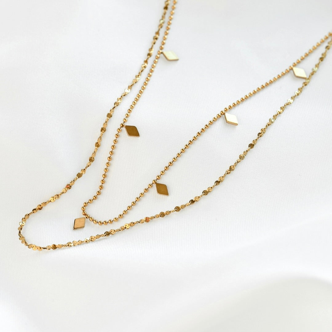Close up view of layered gold necklace with a twisted sparkle chain and ball chain with flat diamond shaped beads.