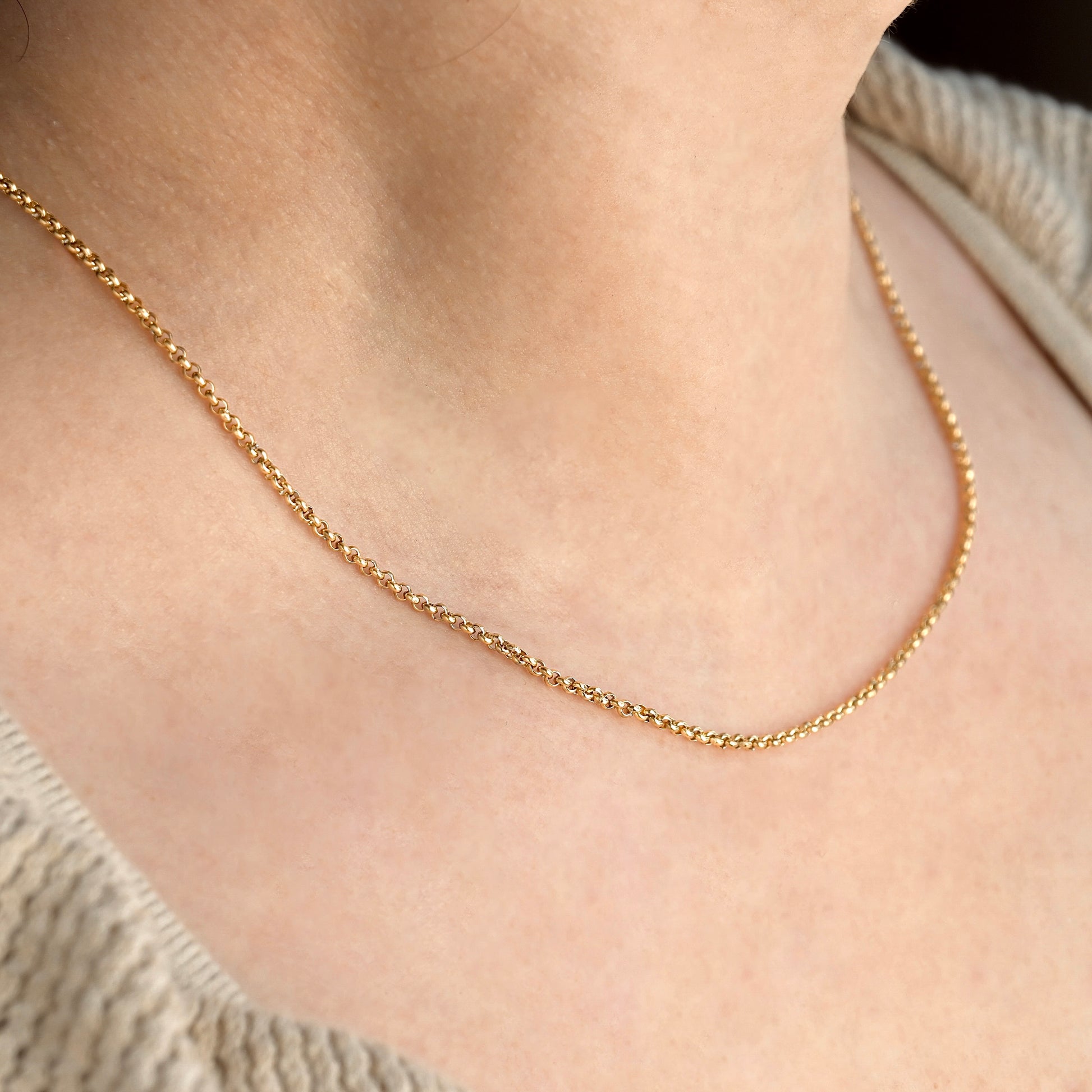 2mm gold rolo chain necklace on a person's neck with a neutral background