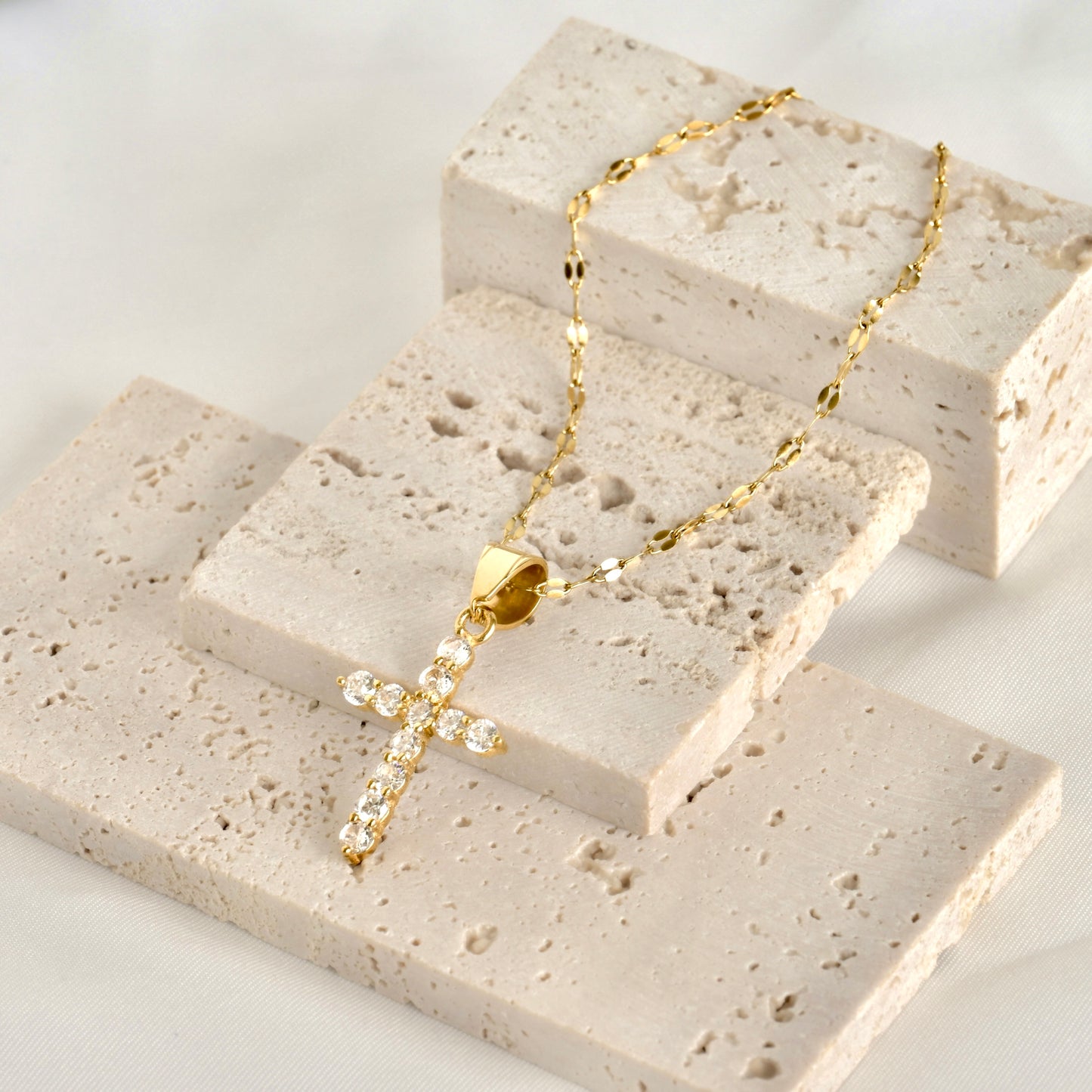 Gold sequin necklace with a cross pendant with clear gemstones on a textured stone surface