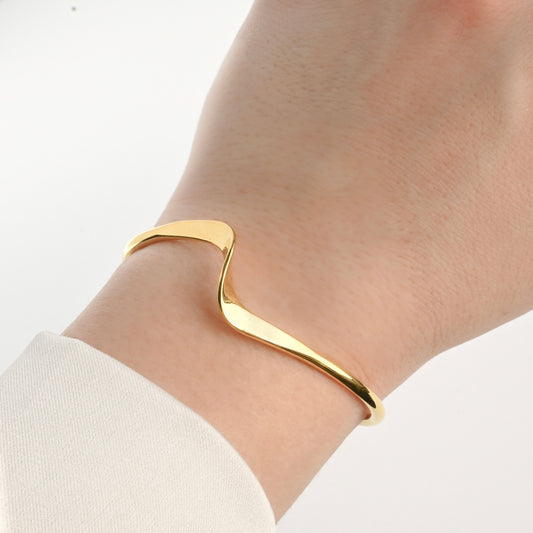 Gold wave cuff bracelet on a wrist with a white background