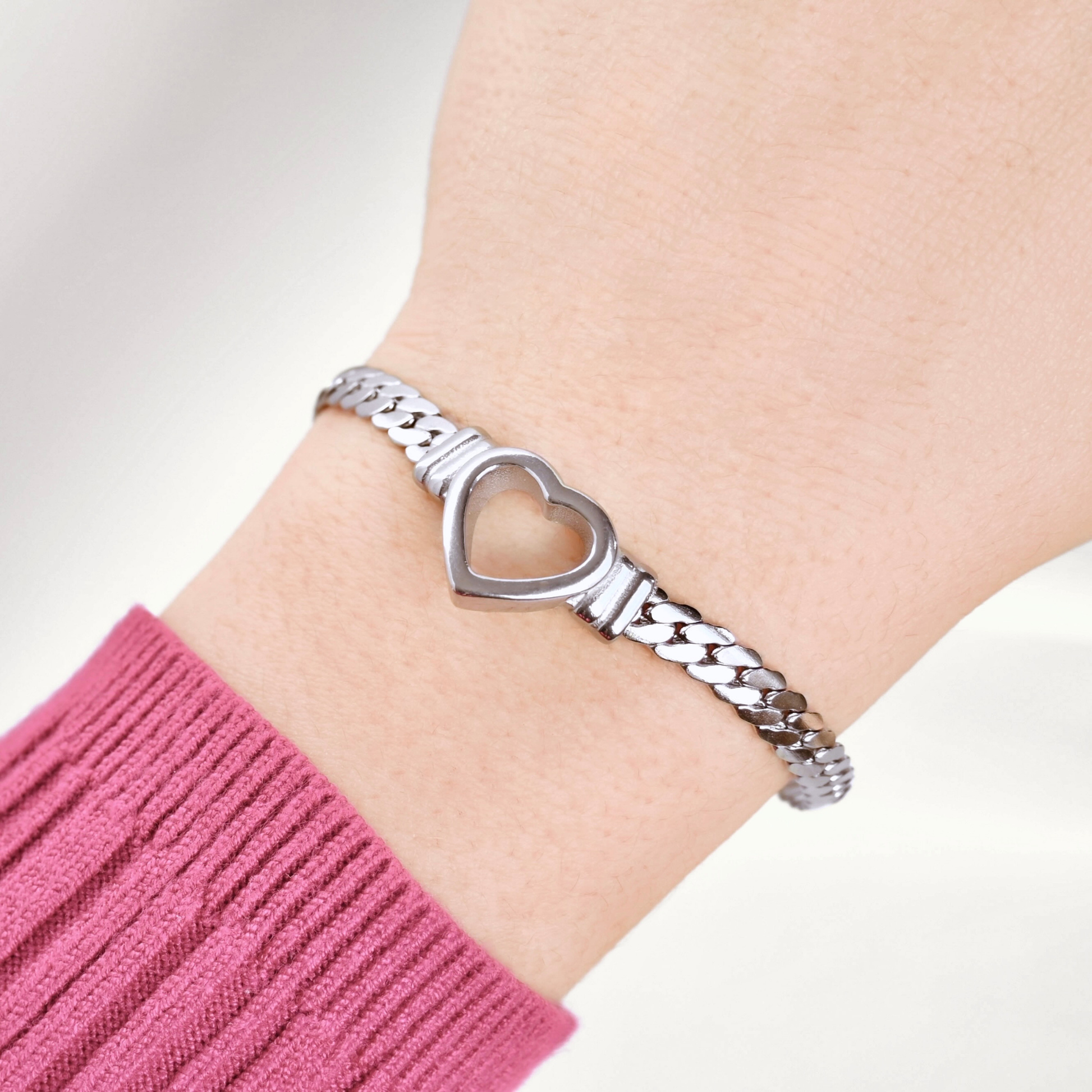 Thick silver  heart bracelet with a snake one chain on a wrist wearing a pink sleeve.