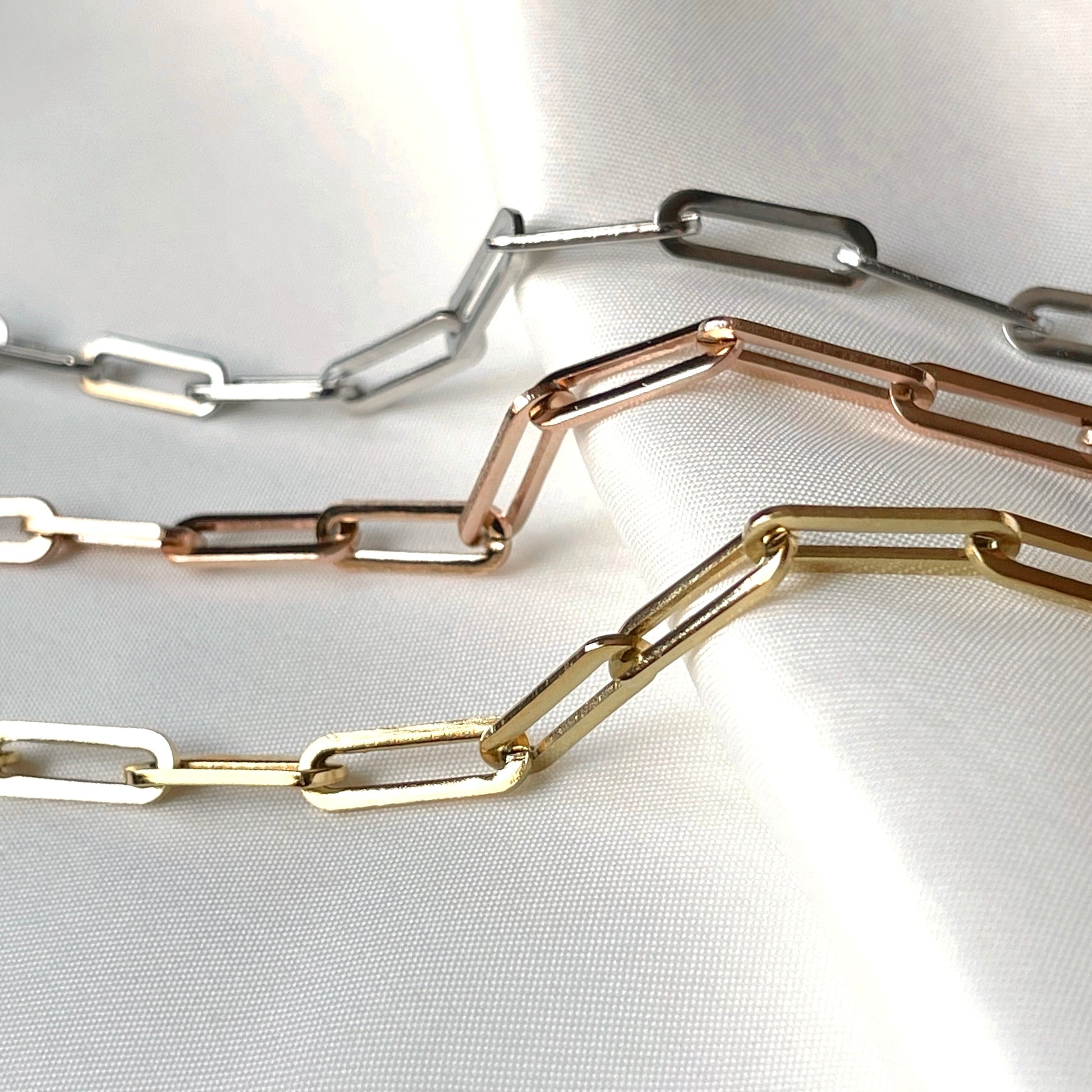 Gold, rose gold, and silver paperclip chain necklaces on a white fabric background