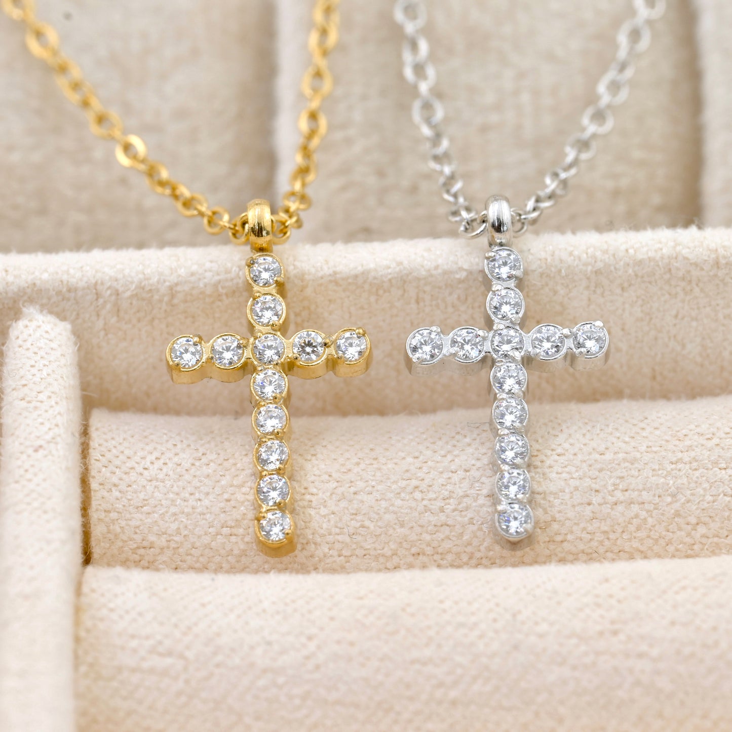 Gold and silver  diamond cross necklaces with clear stones on a beige surface