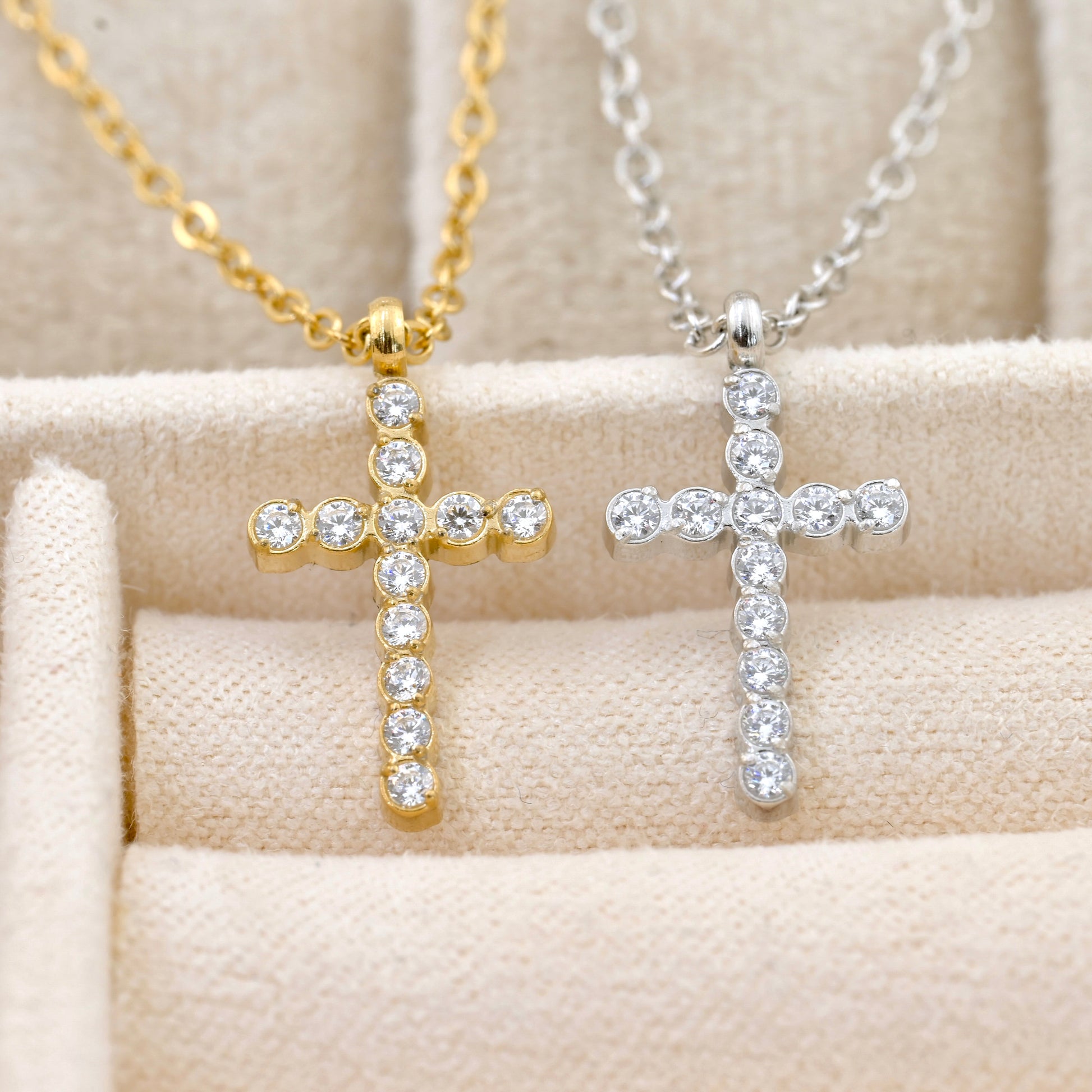 Gold and silver  diamond cross necklaces with clear stones on a beige surface