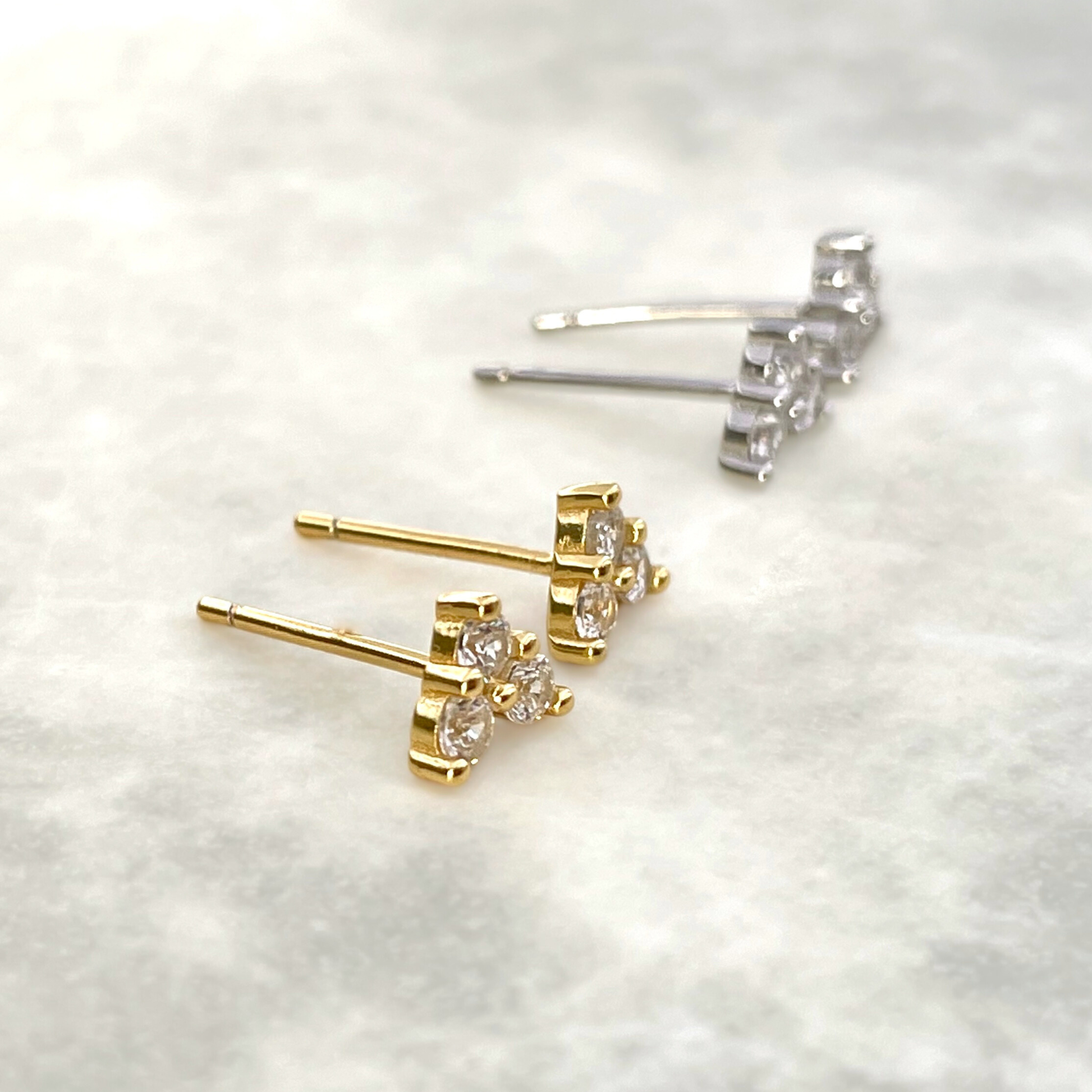 Gold and silver clover stud earrings on a white textured background
