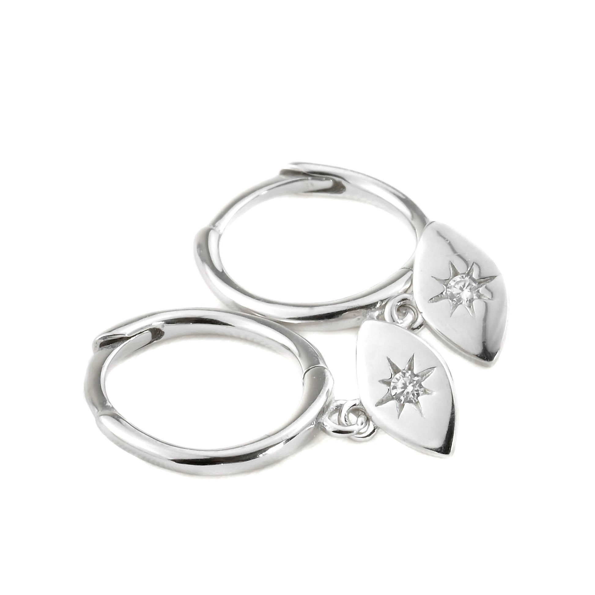Close-up view of silver huggie earrings with evil eye pendants on a white background