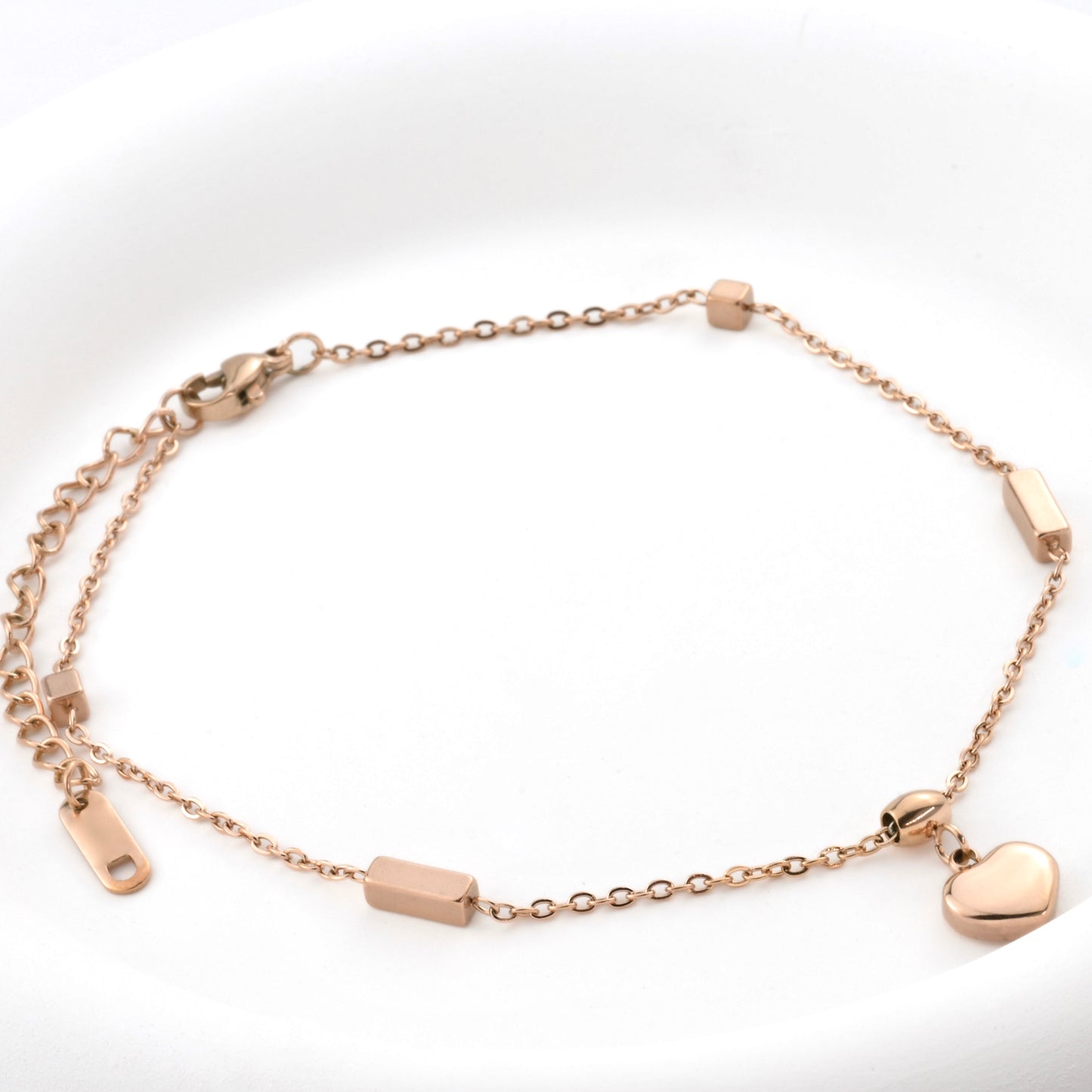 Rose gold bracelet with heart charm, cube and rectangular beads, lobster claw clasp and an extender on a white background