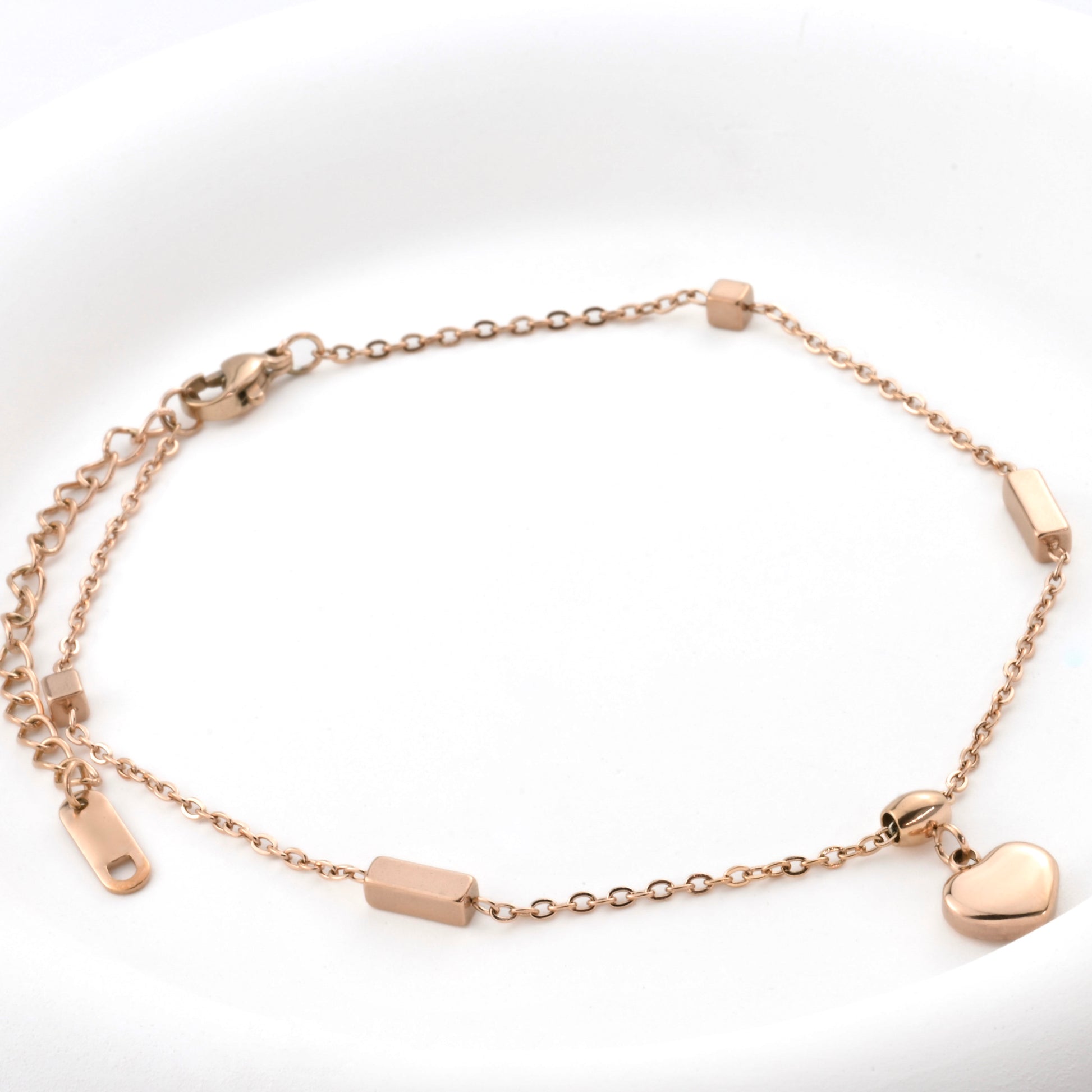 Rose gold bracelet with heart charm, cube and rectangular beads, lobster claw clasp and an extender on a white background