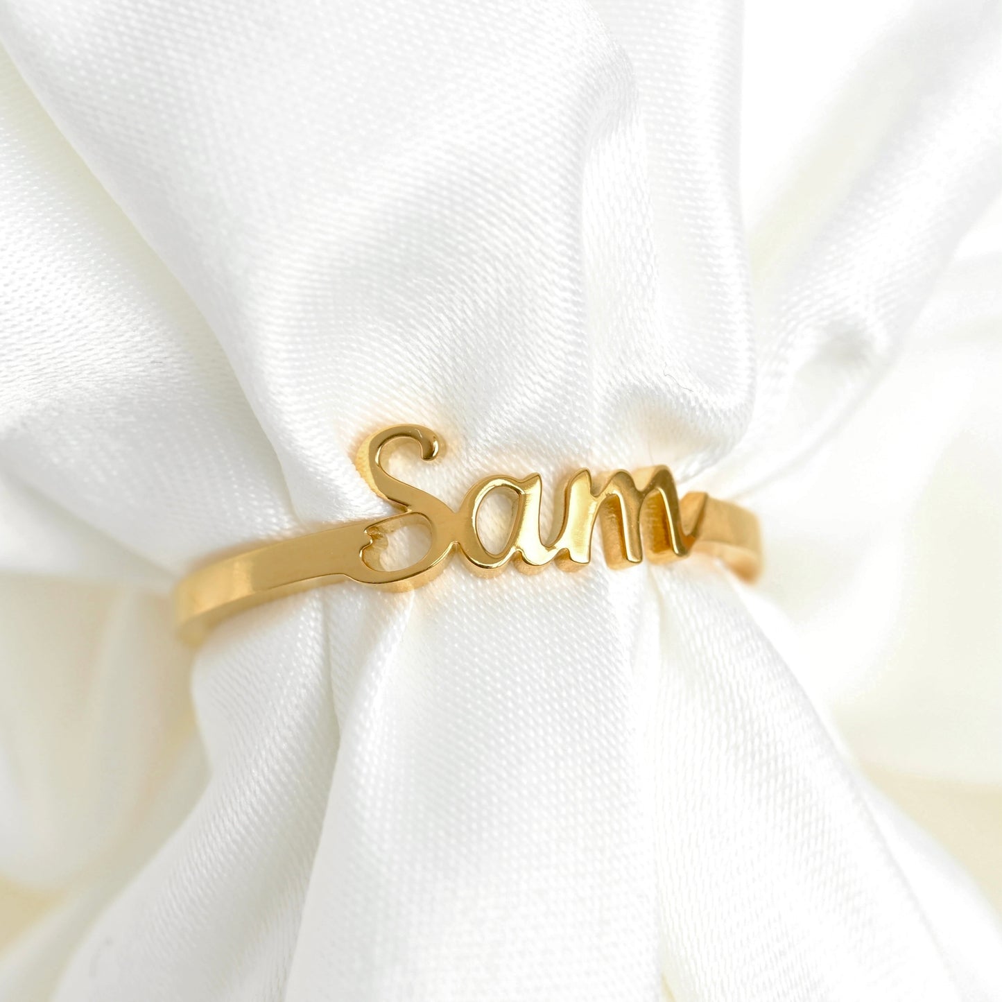 Gold ring with 'Sam' engraving on a white fabric background
