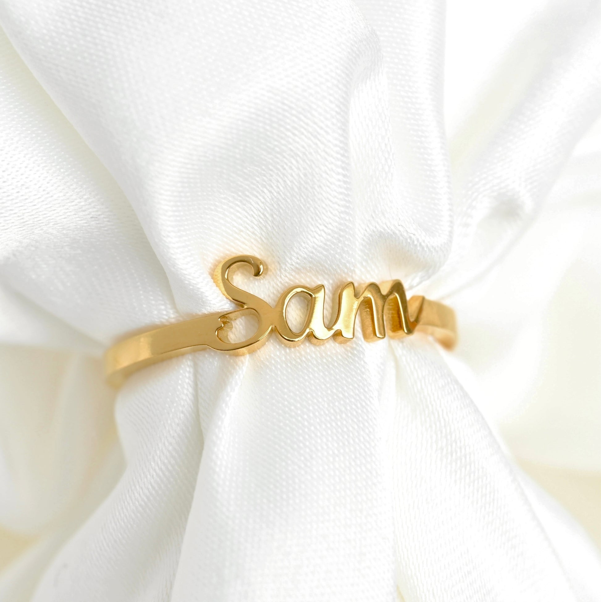 Gold ring with 'Sam' engraving on a white fabric background