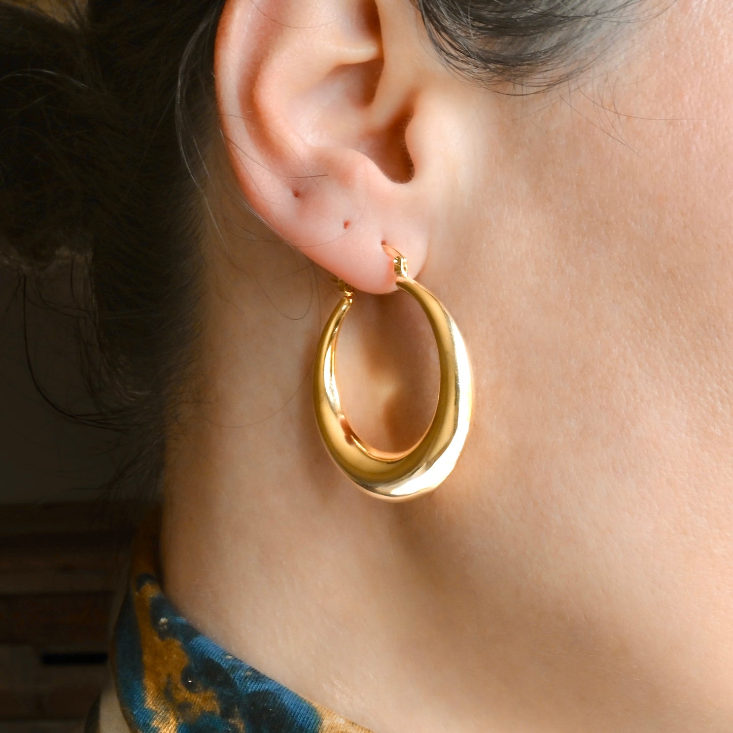 Gold teardrop hoop earrings worn by a person with a blurred background